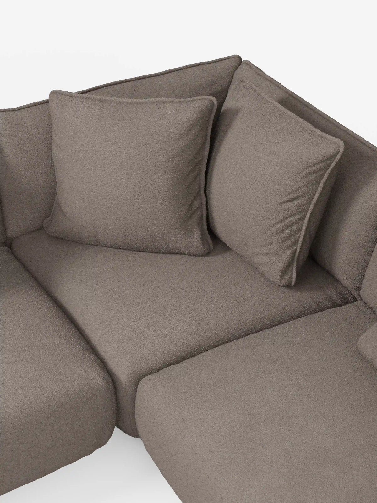 Un primo piano dell'angolo del divano angolare panoramico componibile Nimbus con penisola e angolo in tessuto antimacchia T33 di divitt.sbs, caratterizzato da un morbido rivestimento in tessuto color taupe antimacchia e da due cuscini quadrati per lo schienale. Questo divano componibile Made in Italy si distingue per le linee pulite e arrotondate e l’aspetto confortevole, che risalta sullo sfondo bianco chiaro e uniforme.
