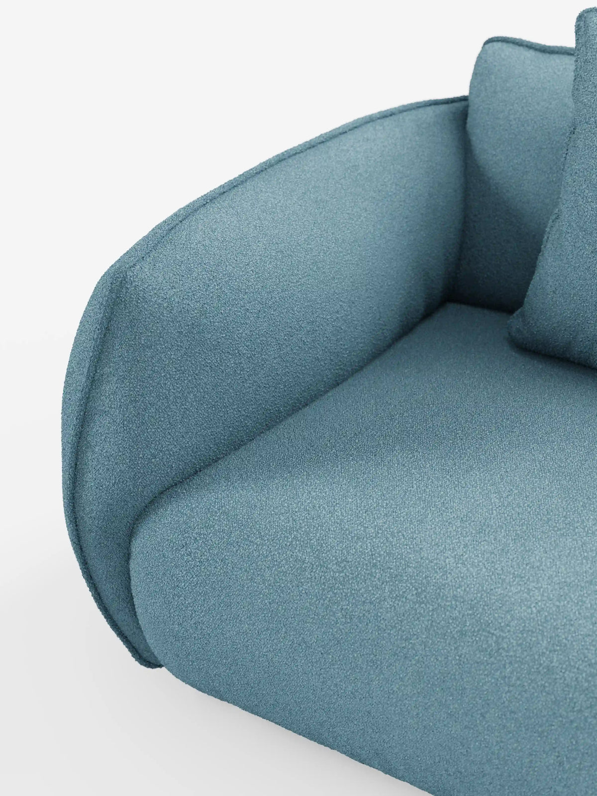 Un primo piano del divano angolare con penisola componibile Nimbus di divitt.sbs, rivestito in morbido tessuto T33 blu con effetto cotone, resistente alle macchie. L'immagine mette in risalto il bracciolo, che si fonde armoniosamente con la seduta e lo schienale, con un cuscino blu coordinato parzialmente visibile su uno sfondo bianco.
