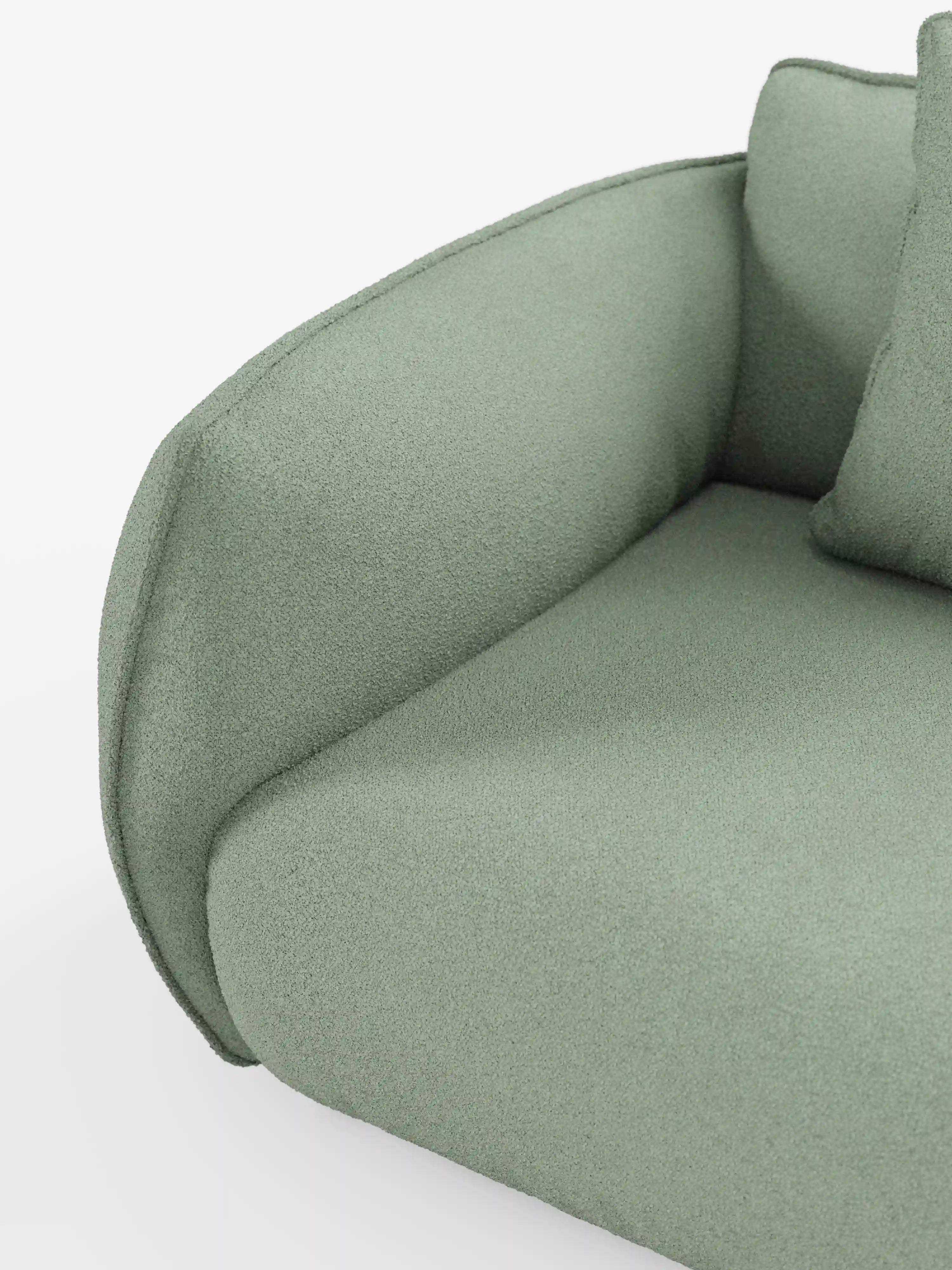 Primo piano del divano angolare con penisola componibile Nimbus di divitt.sbs, rivestito in tessuto T33 resistente alle macchie, color verde salvia chiaro, dall’effetto morbido simile al cotone. Questo divano moderno — noto anche come “divano moderno” — presenta braccioli e cuscini di seduta arrotondati, con una superficie dalla trama delicatamente ruvida. Su uno sfondo bianco minimalista, sul lato destro è visibile una parte di un cuscino coordinato.
