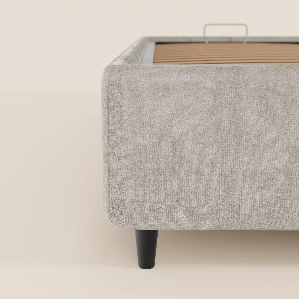 Primo piano della vista laterale del letto sommier imbottito ERON di Letti.store, caratterizzato da un angolo arrotondato, un morbido tessuto impermeabile certificato Oeko-Tex, una gamba verticale in legno nero e doghe interne in legno, su uno sfondo color crema.