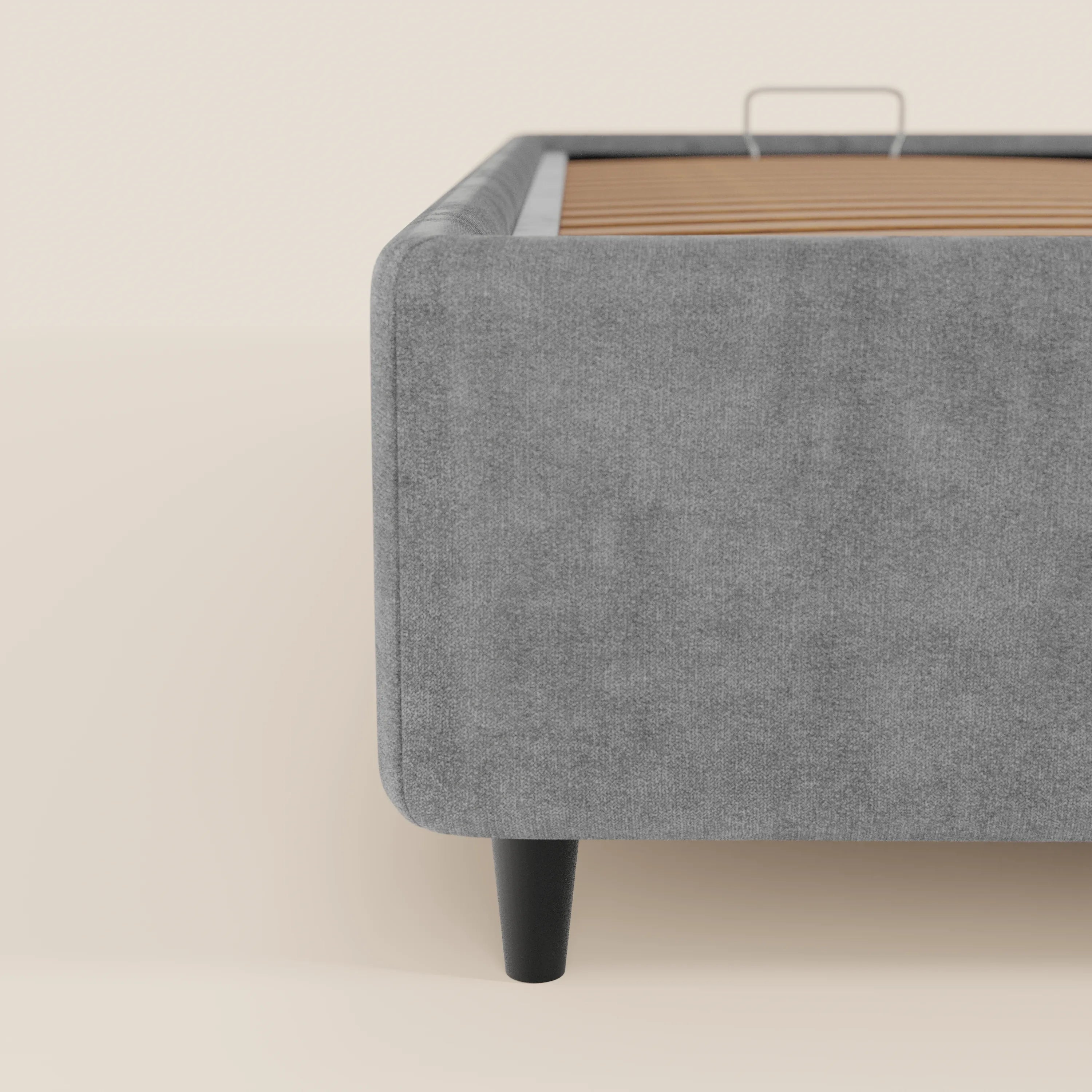 Una vista parziale del letto sommier imbottito ERON di Letti.store, caratterizzato da un tessuto impermeabile certificato Oeko-Tex, gambe affusolate nere e doghe in legno a vista, su uno sfondo beige chiaro.