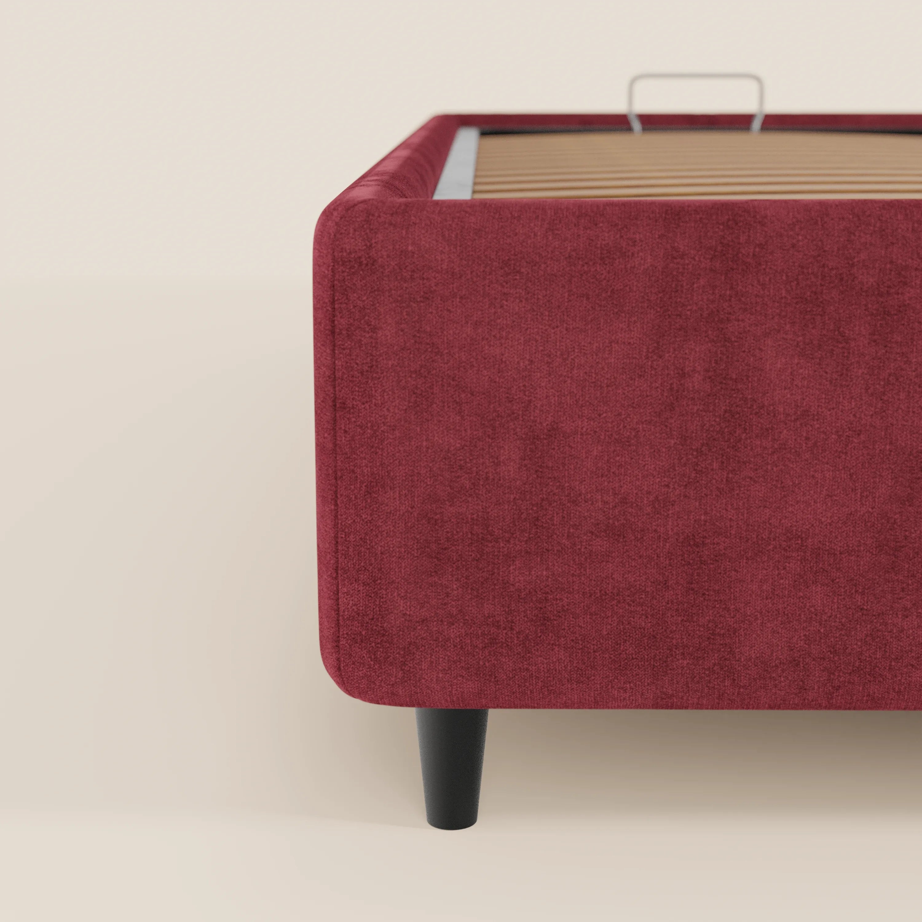 Un primo piano del letto sommier imbottito ERON di Letti.store, rivestito in tessuto impermeabile certificato Oeko-Tex, mostra l'angolo sinistro con le sue linee pulite, le gambe affusolate nere, le doghe in legno a vista e uno sfondo chiaro e neutro.