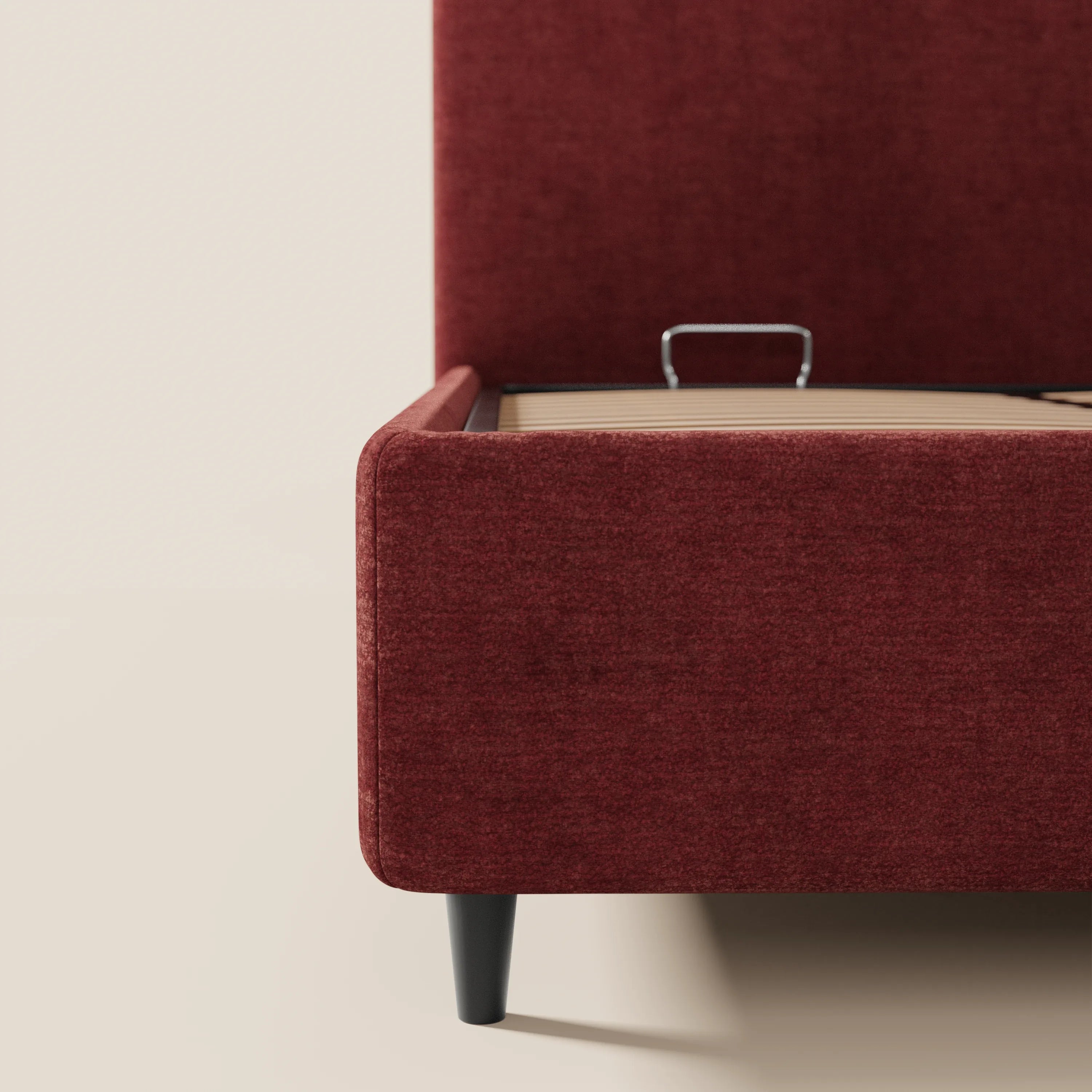 Un primo piano del letto KAELOS minimal imbottito di Letti.store, in ciniglia rosso scuro, ne mette in risalto le gambe alte nere, le doghe in legno e lo spazio contenitivo. La parete e il pavimento chiari esaltano il suo design pulito e moderno, caratterizzato da una testiera arrotondata.