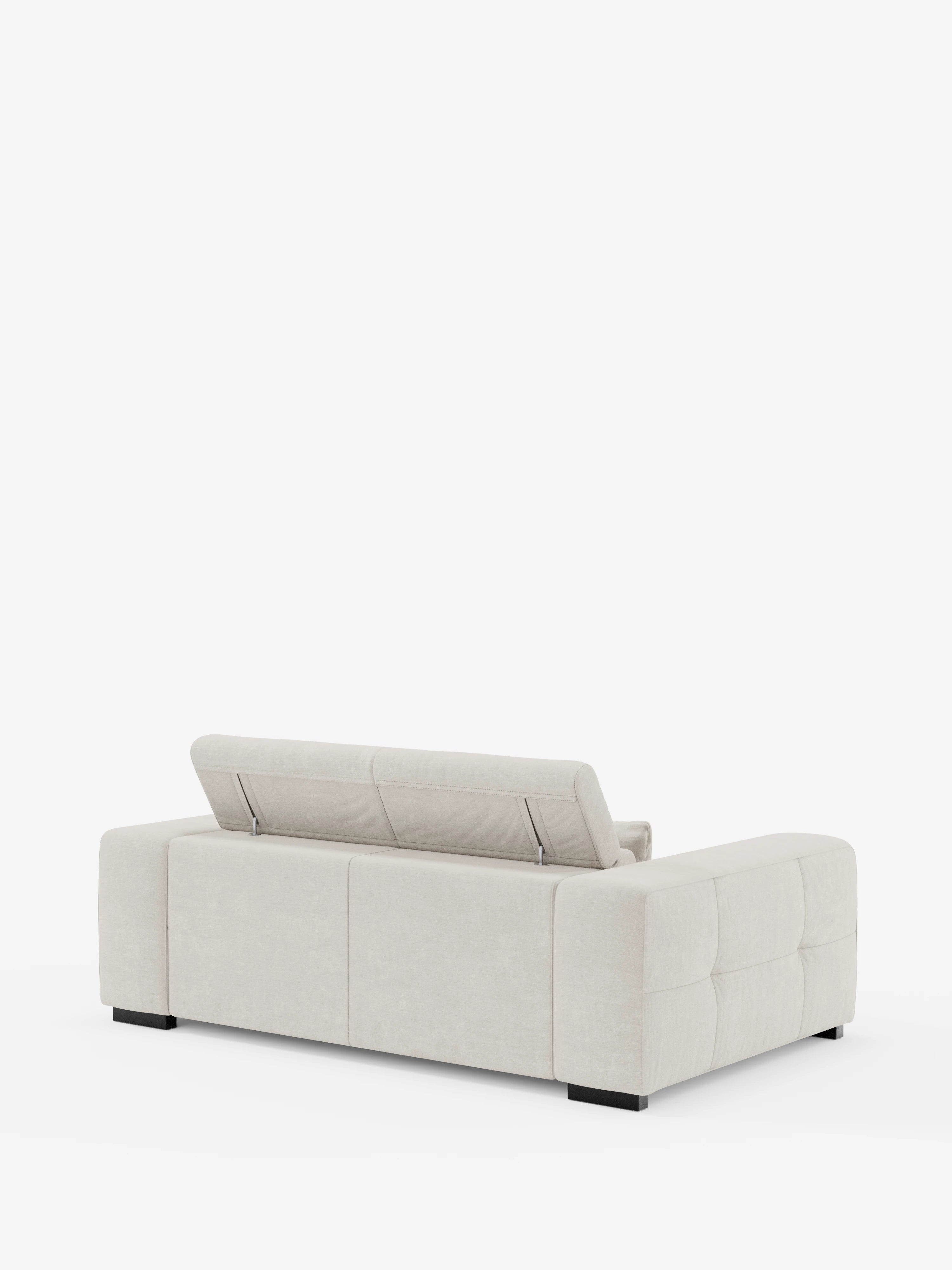 Un moderno divano Monarch color beige chiaro di divitt.sbs visto da dietro; questo «Divano con relax elettrico per l’allungamento delle sedute e poggiatesta reclinabile in tessuto morbido smacchiabile T31» presenta un profilo basso, ampi braccioli imbottiti, piedini a blocco neri, fianchi trapuntati e un poggiatesta regolabile parzialmente sollevato sul lato sinistro dello schienale.