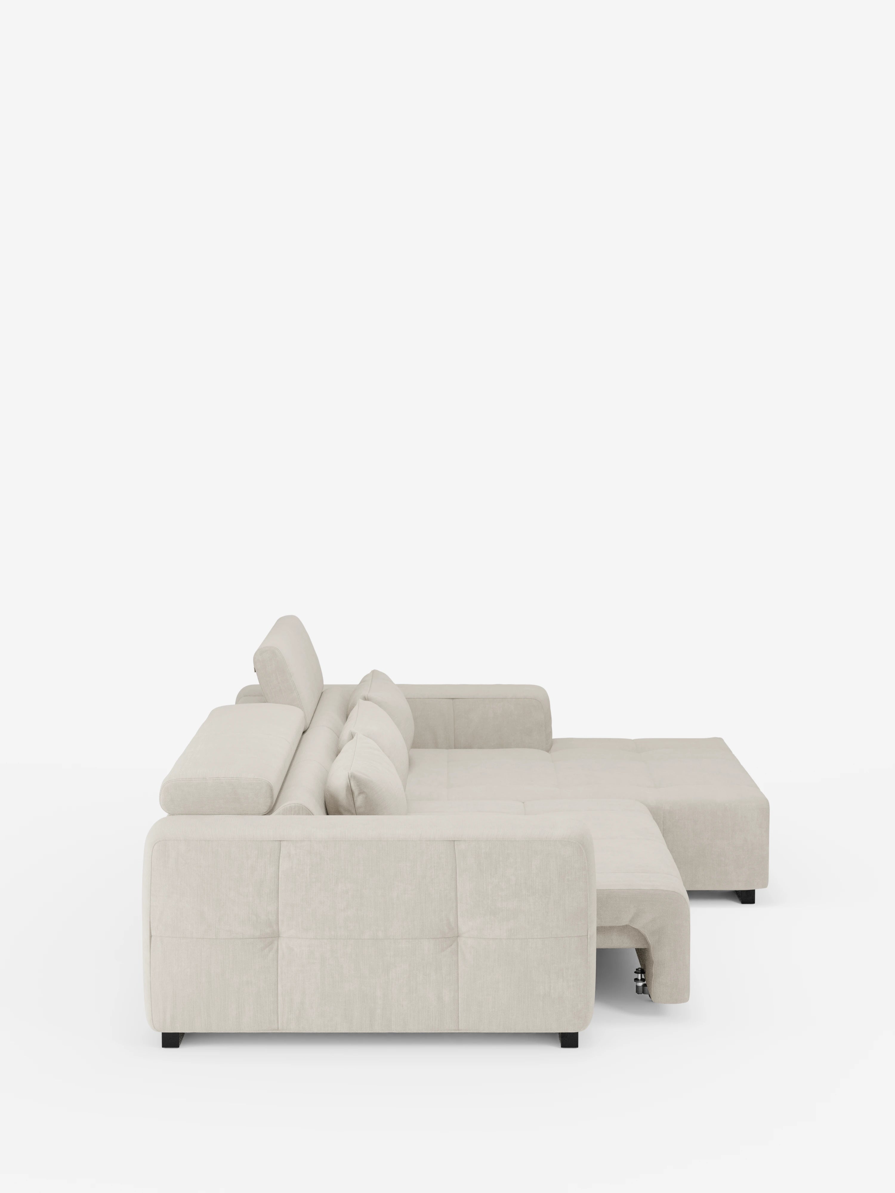 Una vista laterale mostra il divano angolare Monarch con penisola e funzione Relax Elettrico per l’allungamento delle sedute di divitt.sbs, caratterizzato da un design moderno in beige chiaro con cuscini di seduta trapuntati e poggiatesta reclinabili regolabili. La sezione chaise allungata e le gambe basse nere risaltano chiaramente sullo sfondo bianco a tinta unita. Rivestito in morbido tessuto T31 resistente alle macchie.