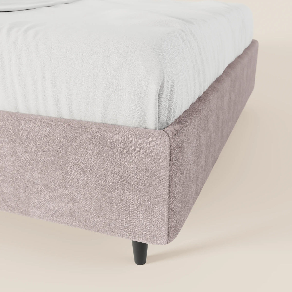 Un primo piano del letto sommier imbottito ERON di Letti.store ne mette in risalto il tessuto impermeabile Oeko-Tex color malva chiaro e le gambe nere affusolate. Il letto, progettato senza testiera e dotato di contenitore, presenta un lenzuolo con angoli bianco su uno sfondo color crema chiaro.