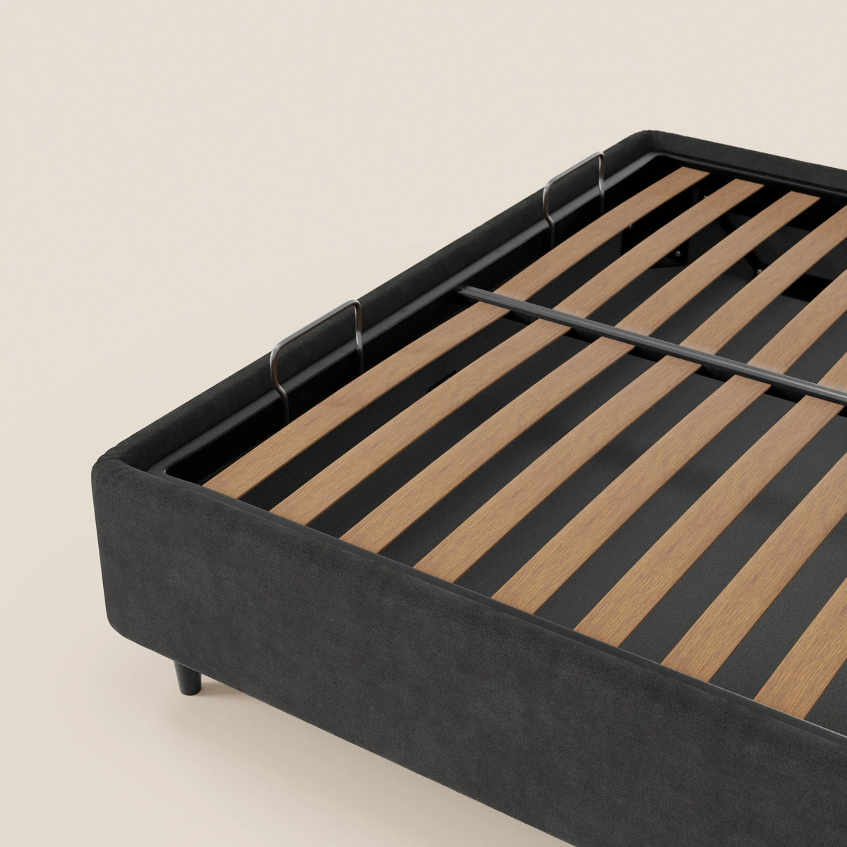 Un primo piano mostra il letto sommier imbottito con vano contenitore ERON di Letti.store, realizzato con tessuto impermeabile certificato Oeko-Tex, doghe in legno, barre di sostegno in metallo e gambe corte nere, su uno sfondo chiaro a tinta unita.