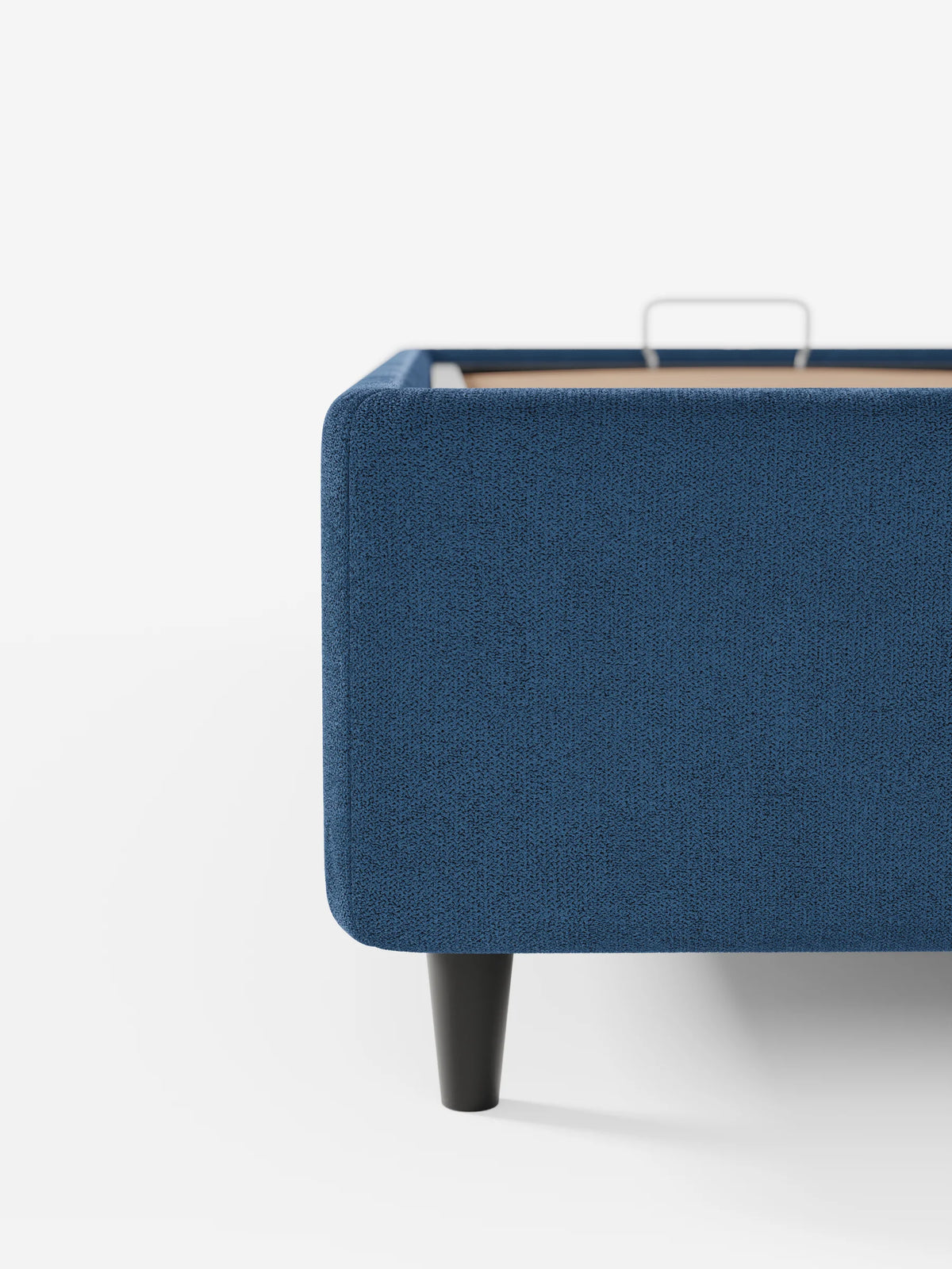 Primo piano dell'angolo di un letto sommier imbottito ERON blu navy con vano contenitore in tessuto impermeabile certificato Oeko-Tex, caratterizzato da una finitura testurizzata, una gamba affusolata scura e una maniglia in metallo per il vano contenitore.