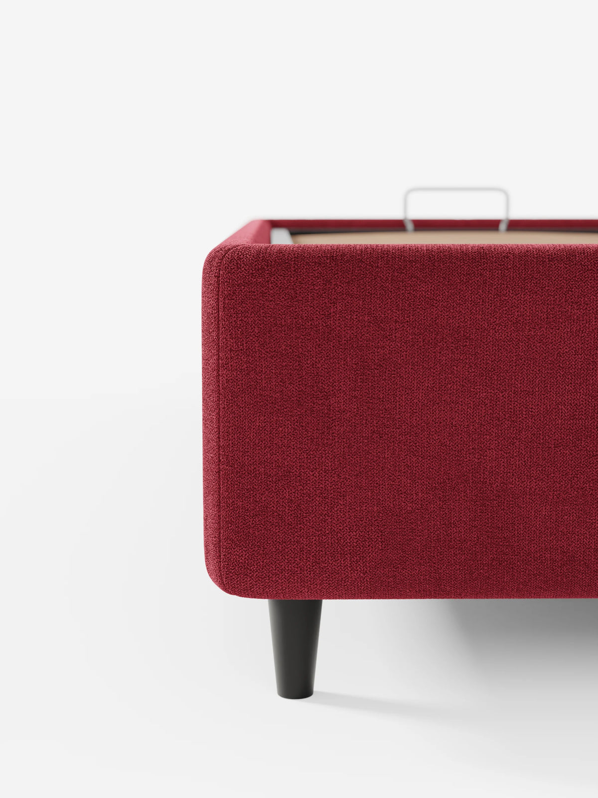 Primo piano dell'angolo di un letto sommier imbottito ERON color bordeaux con vano contenitore in tessuto impermeabile certificato Oeko-Tex, che mostra una robusta gamba scura e il meccanismo di stivaggio interno su uno sfondo bianco a tinta unita.