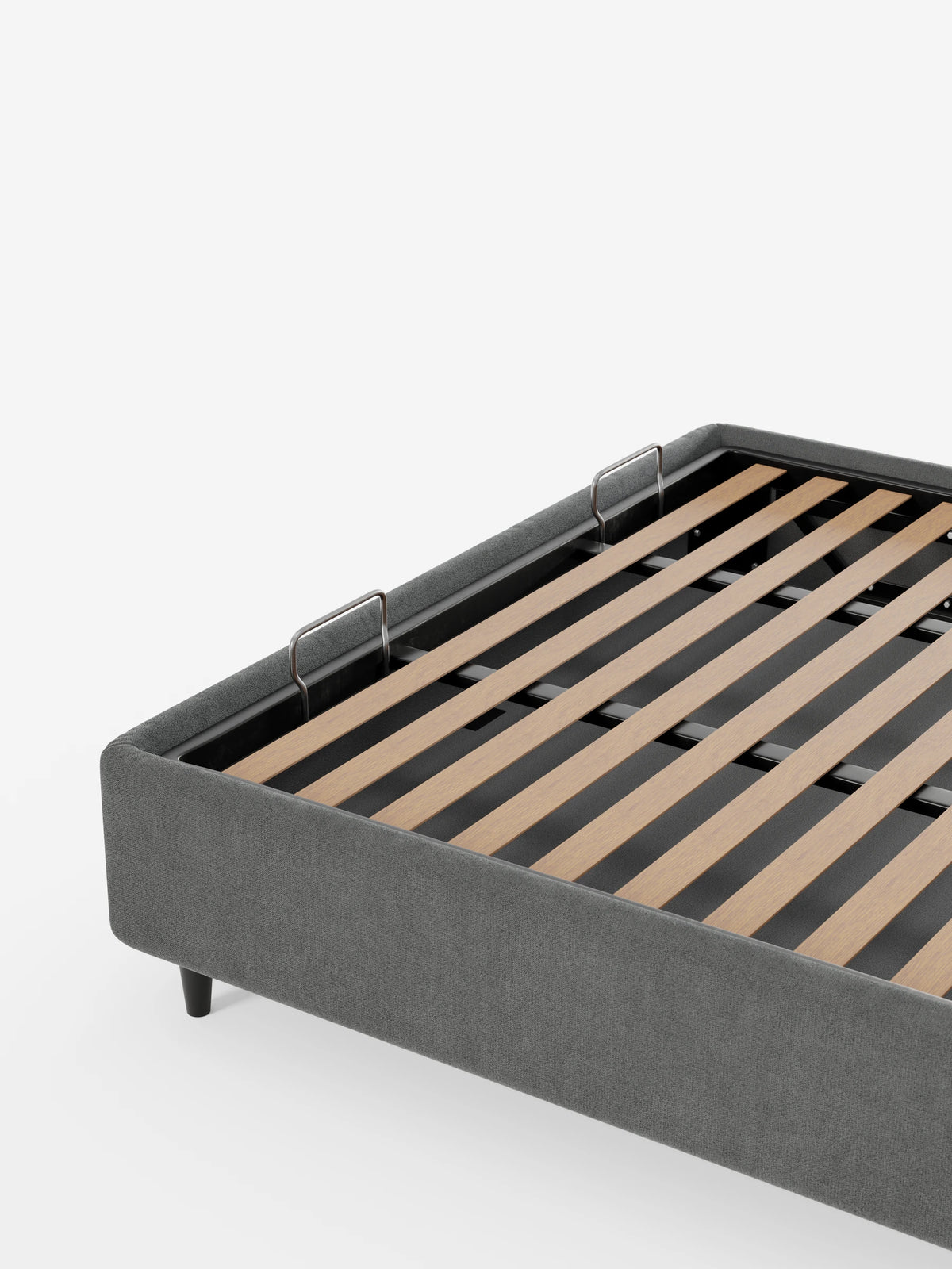 Il letto sommier imbottito ERON con contenitore in tessuto impermeabile certificato Oeko-Tex è un letto imbottito grigio con doghe in legno chiaro, piedini corti scuri e due maniglie metalliche sulla base per sollevarlo.