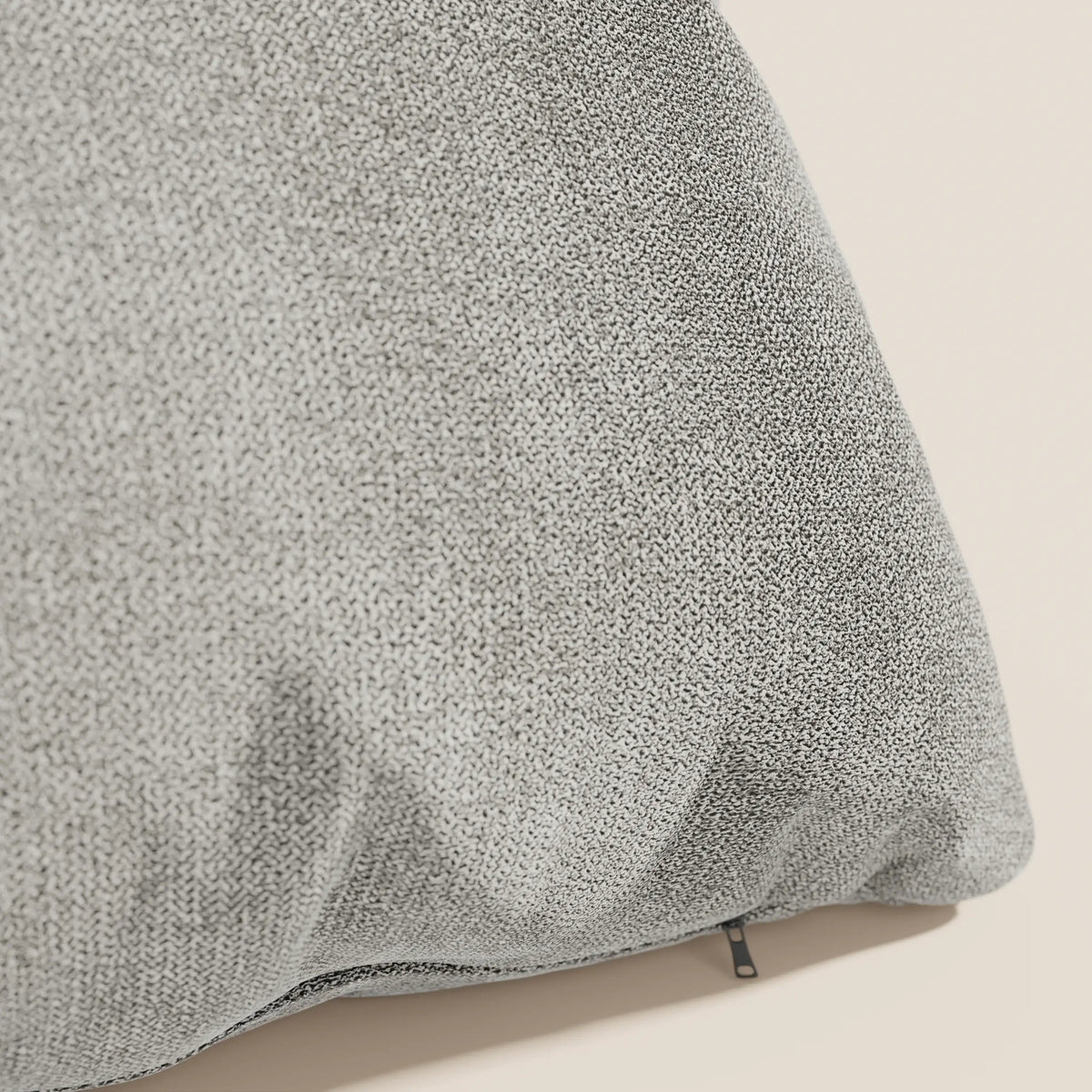 Primo piano del cuscino Destiny 45x45 cm di divitt.sbs in morbido tessuto impermeabile T02 beige con trama a vista e piccola cerniera nera nell'angolo in basso a destra, appoggiato su una superficie beige chiaro.