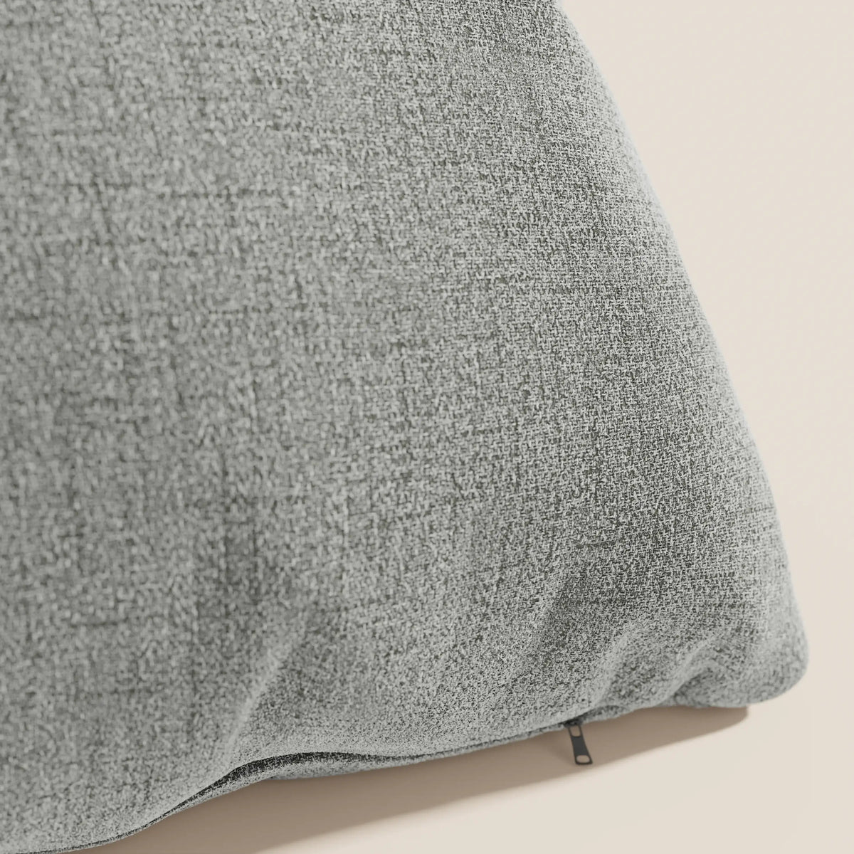 Primo piano del cuscino Felis di divitt.sbs in T03 grigio chiaro, realizzato in morbido tessuto idrorepellente, caratterizzato da una piccola cerniera nera sul bordo inferiore su uno sfondo beige chiaro.
