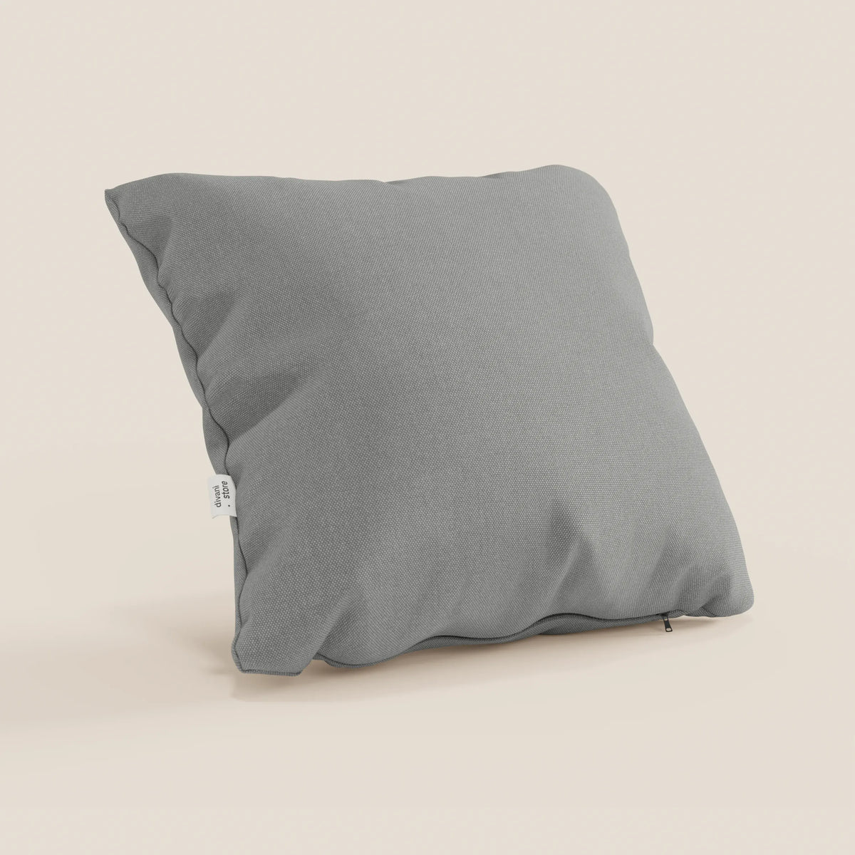 Un cuscino Honey quadrato 45x45 cm di divitt.sbs in T13 grigio tessuto simil cotone impermeabile si trova in posizione verticale su uno sfondo beige, con bordi leggermente stropicciati, trama del tessuto visibile, una piccola etichetta laterale bianca e una cerniera inferiore nascosta.