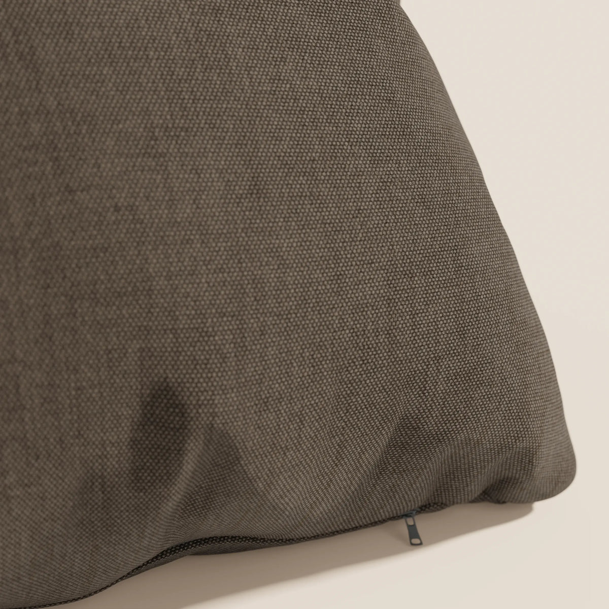 Primo piano del cuscino Honey 45x45 cm di divitt.sbs in tessuto marrone simil cotone impermeabile T13, con una cerniera visibile su una cucitura e una sottile macchia più scura in basso a sinistra, su uno sfondo bianco sporco.