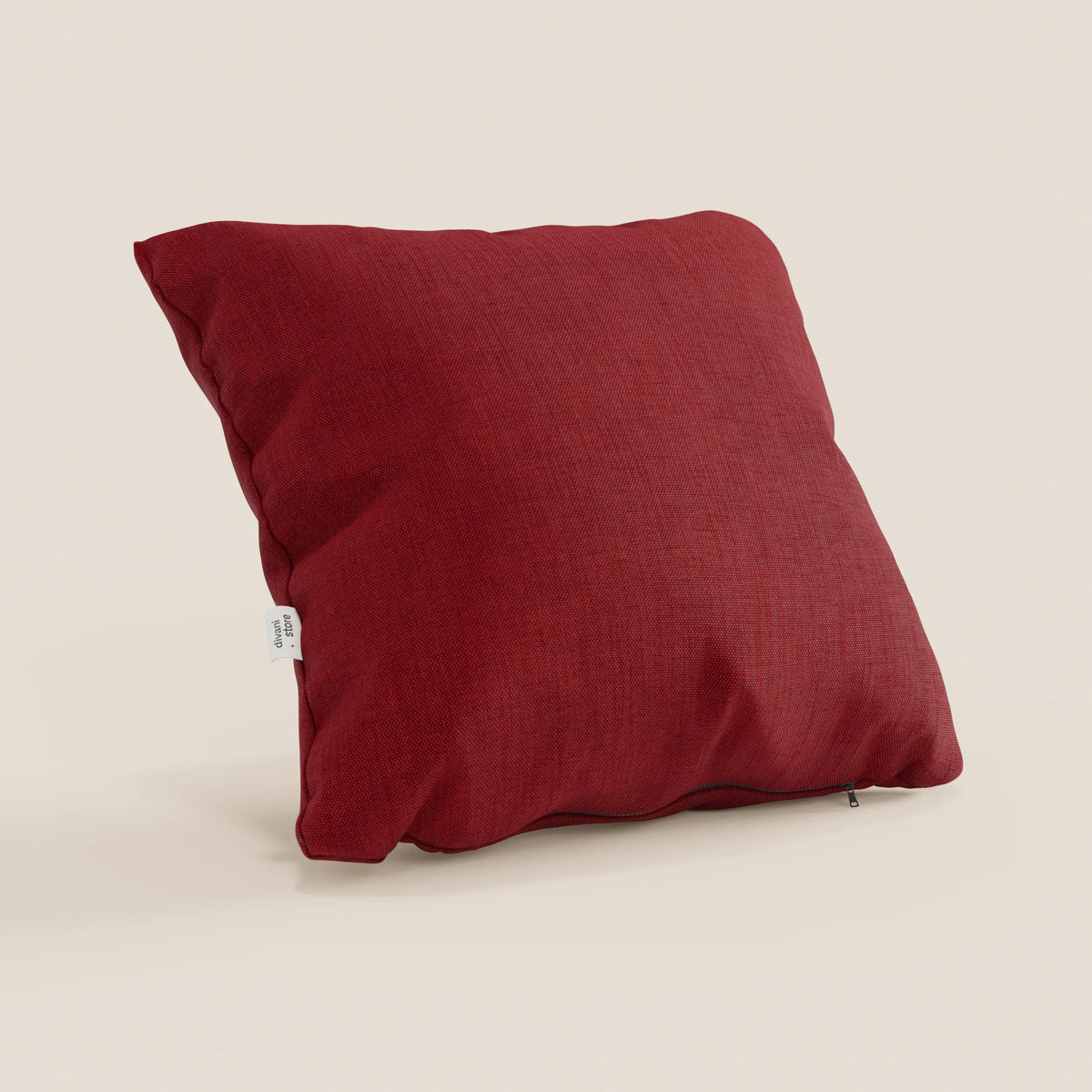 Un cuscino Honey di divitt.sbs, 45x45 cm in T13 rosso simil cotone impermeabile, poggia su una superficie beige. Presenta un sottile rivestimento effetto cotone, una piccola etichetta bianca sul lato e una cerniera lungo il bordo inferiore.