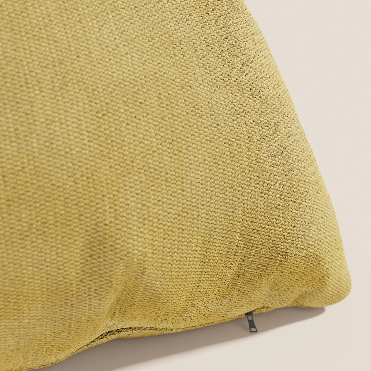 Primo piano del cuscino Miami 45x45 cm in T14 giallo di divitt.sbs, realizzato in morbido tessuto impermeabile con motivo intrecciato e tirazip nero, su sfondo beige chiaro.