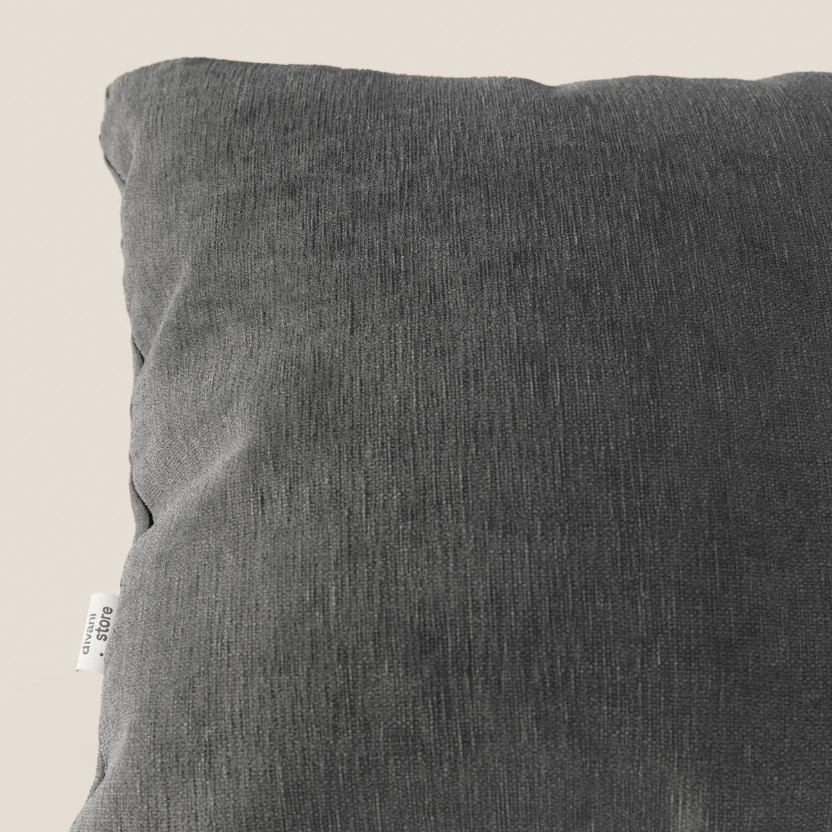 Primo piano del cuscino Bolero di divitt.sbs in grigio scuro, con tessuto T31 morbido, strutturato e antimacchia. Una piccola etichetta bianca con testo nero è cucita nella cucitura sinistra. Lo sfondo è una tonalità neutra di beige chiaro.