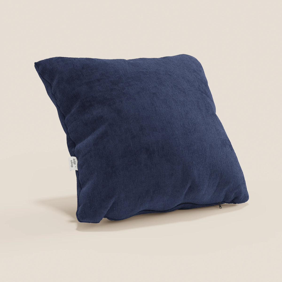 Il cuscino Bolero di divitt.sbs, qui in blu scuro con tessuto morbido T31 resistente alle macchie, impermeabile e irrestringibile, è quadrato e presenta un'etichetta bianca laterale. Sullo sfondo c'è una parete beige chiara.