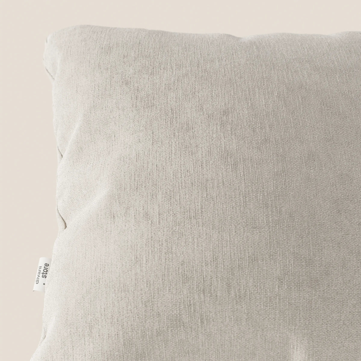 Primo piano del cuscino Bolero di divitt.sbs in grigio chiaro, con una piccola etichetta bianca sulla cucitura sinistra. Realizzato in morbido tessuto T31 antimacchia, impermeabile e non restringente. Su uno sfondo beige neutro.