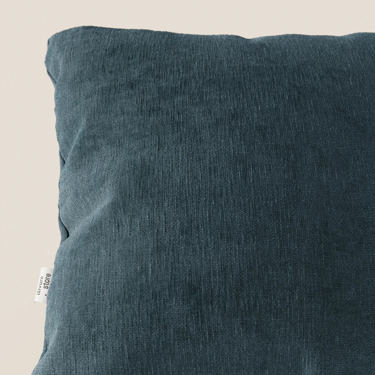 Primo piano del cuscino Bolero di divitt.sbs in colore verde scuro, caratterizzato da un morbido tessuto T31 antimacchia, impermeabile e non restringente. Una piccola etichetta bianca appare a sinistra su uno sfondo beige chiaro che evidenzia il cuscino.