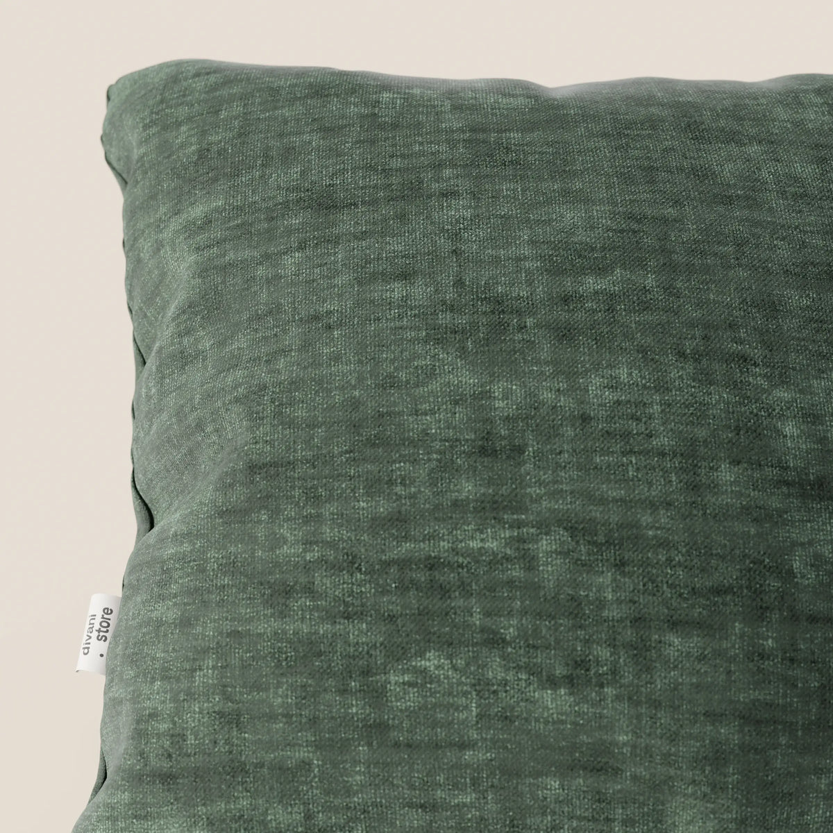 Primo piano del cuscino Sofia di divitt.sbs in verde scuro, realizzato in morbido velluto nuvolato impermeabile e antimacchia (Easy Clean T35), con etichetta bianca sul lato. Lo sfondo bianco sporco mette in risalto la consistenza felpata e i dettagli sottili.