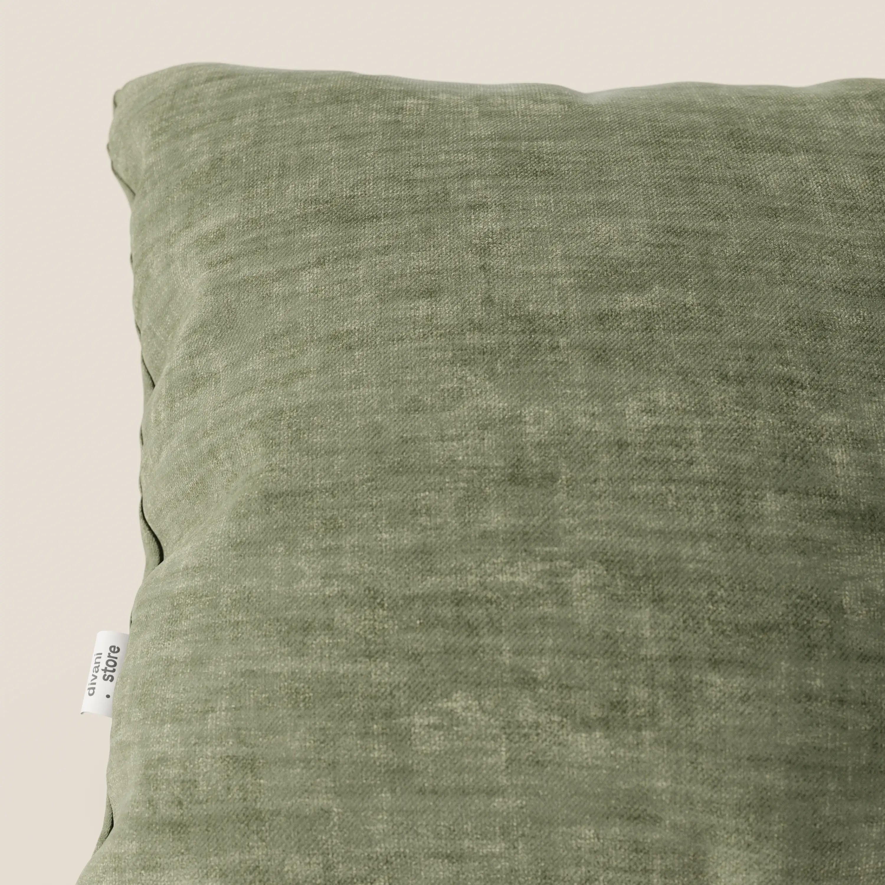 Primo piano del cuscino Sofia di divitt.sbs, realizzato in morbido velluto verde nuvolato (Easy Clean T35), caratterizzato da una piccola etichetta bianca con testo nero sulla cucitura sinistra. Lo sfondo è bianco sporco e si vede solo una parte del cuscino.