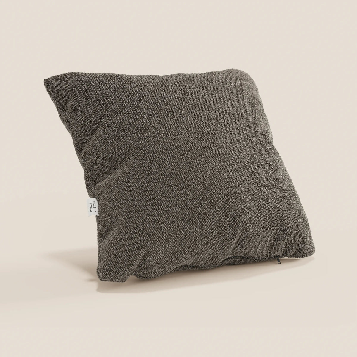 Un cuscino Lambada quadrato di colore marrone scuro di divitt.sbs, realizzato in tessuto T33 lavabile e impermeabile simile al cotone fresco, si trova in posizione obliqua su uno sfondo beige chiaro. Una piccola etichetta bianca è attaccata sul lato, con una cerniera visibile sul bordo inferiore.