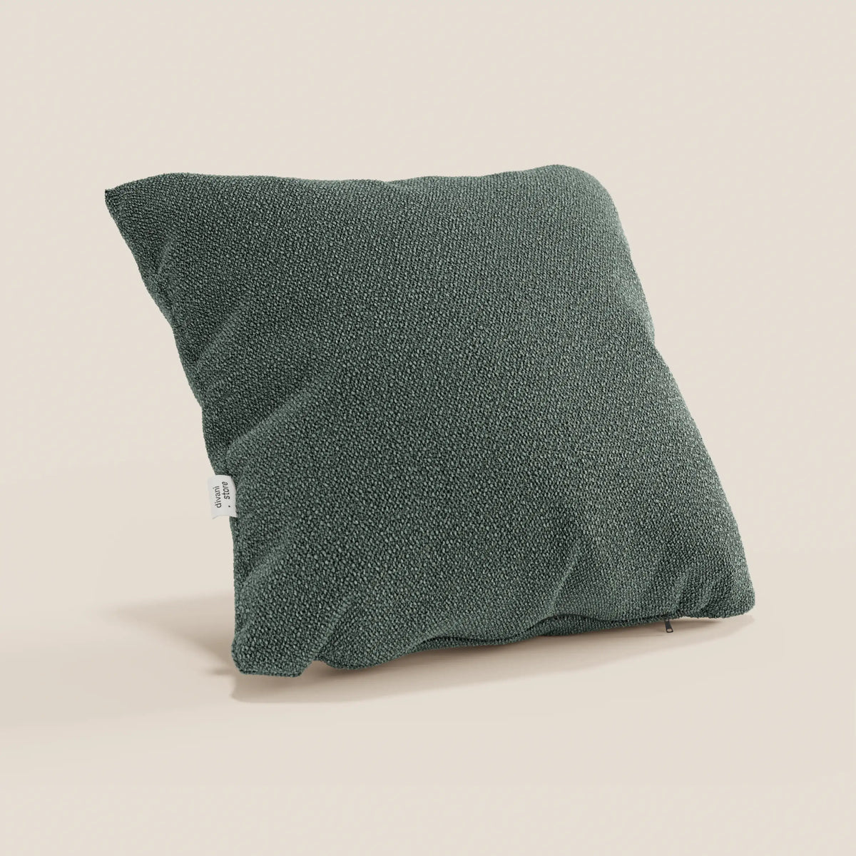 Un cuscino Lambada quadrato verde scuro di divitt.sbs è presentato su uno sfondo beige chiaro. Realizzato in tessuto T33 naturale, antimacchia e impermeabile, ha una superficie morbida che lascia intravedere un'imbottitura in peluche e presenta una piccola etichetta laterale bianca.
