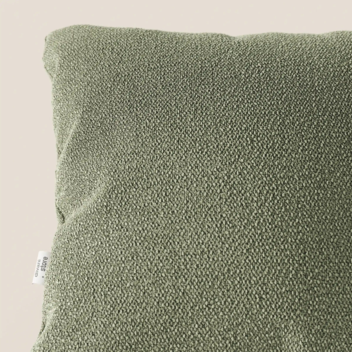 Primo piano del cuscino Lambada di divitt.sbs in verde oliva, realizzato in tessuto fresco e naturale T33 antimacchia e impermeabile, visto dall'alto su sfondo beige con etichetta bianca visibile in basso a sinistra.