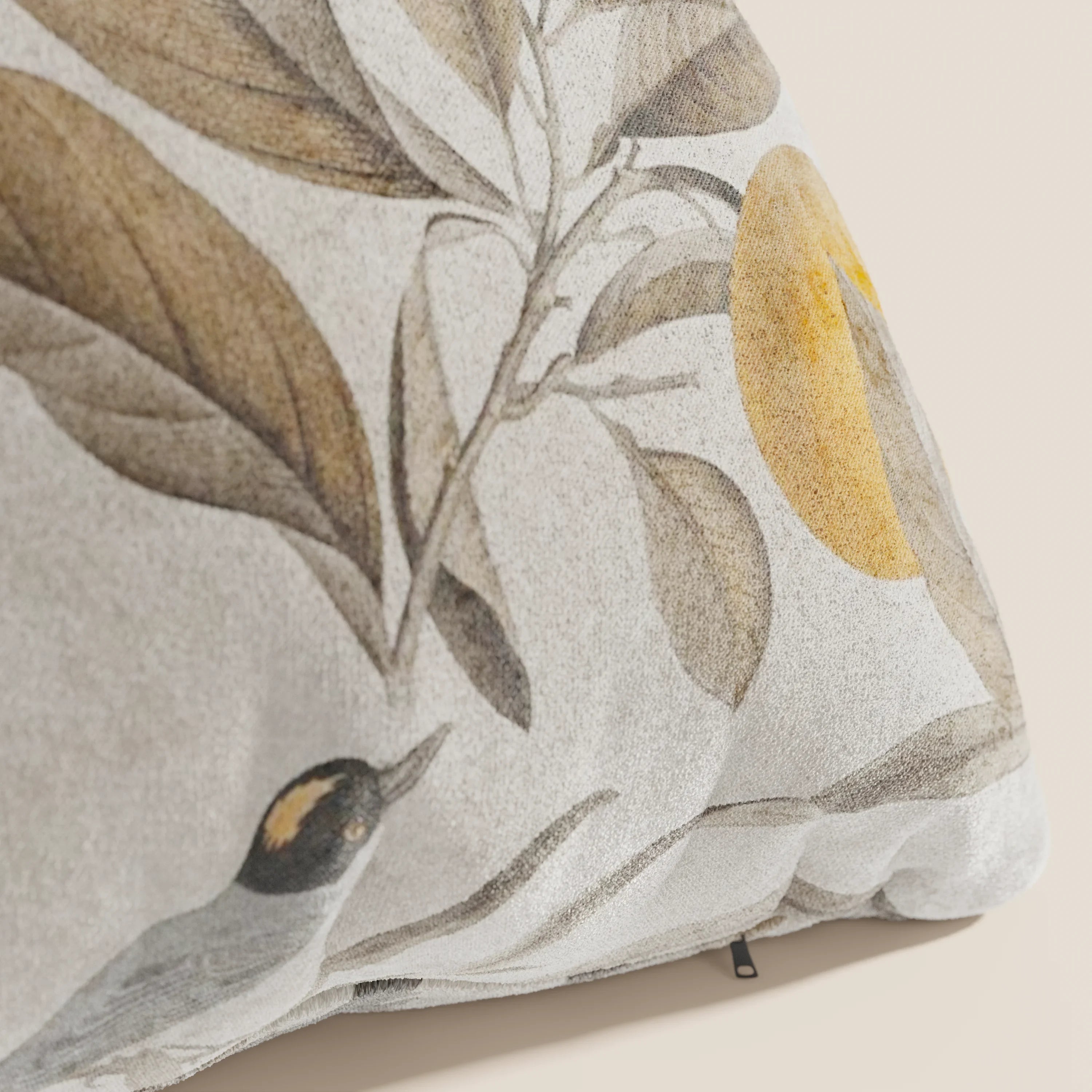 Primo piano di Lemon elegante collezione di cuscini a fantasia in velluto impermeabile beige di divitt.sbs, con foglie marroni, un sole o una luna gialli e un uccello giallo e nero per un look ispirato alla natura nei toni tenui della terra.