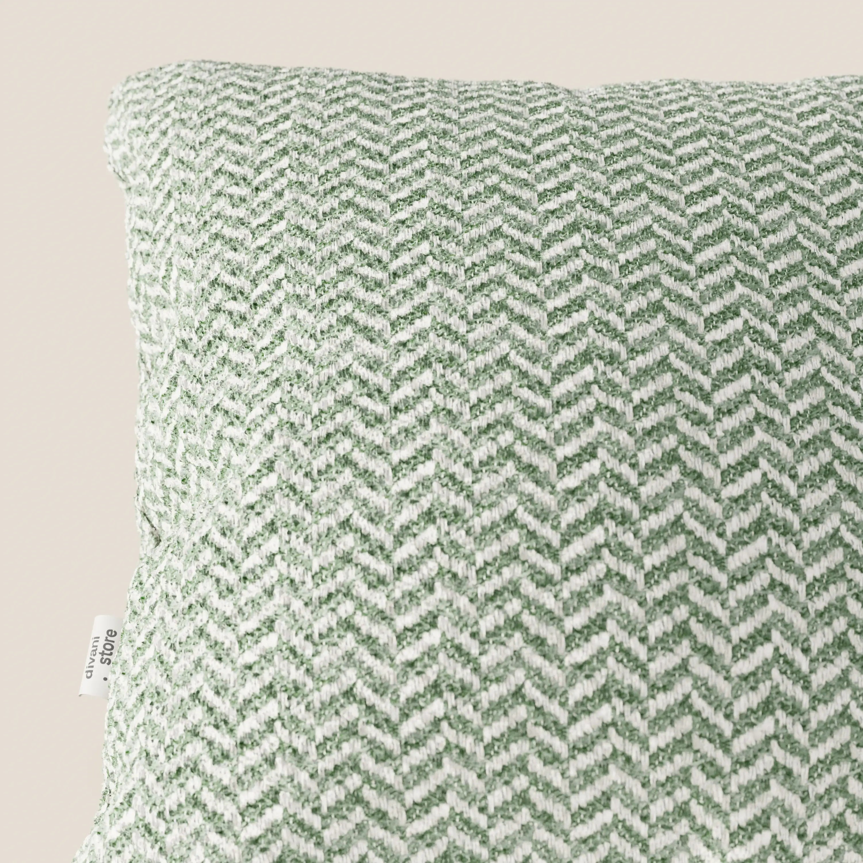 Un primo piano del cuscino Sorrento 45x45 in Lino di divitt.sbs ne mette in risalto il motivo a chevron intrecciato verde e bianco, il tessuto testurizzato e l'etichetta in tessuto sul bordo sinistro. Lo sfondo beige chiaro esalta questo elegante cuscino lavabile in lavatrice.