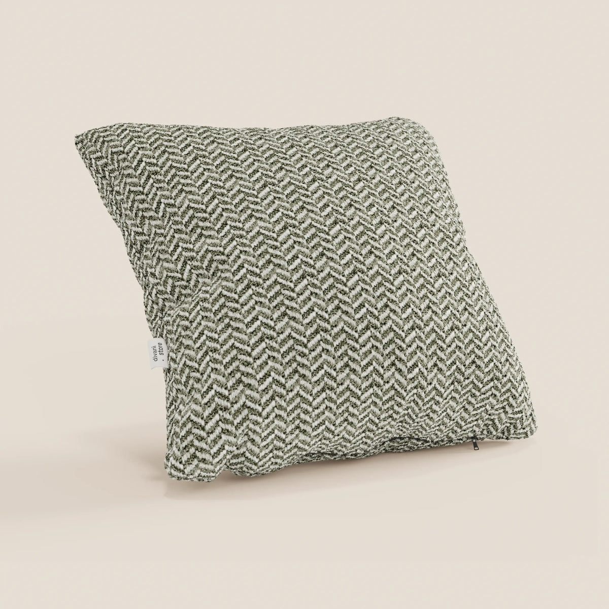 Il cuscino Sorrento 45x45 in lino | Eleganza Naturale di divitt.sbs presenta un motivo a spina di pesce in rilievo nei toni del verde scuro e del bianco sporco, ripreso di sbieco con l'etichetta del tessuto su uno sfondo beige chiaro a tinta unita.
