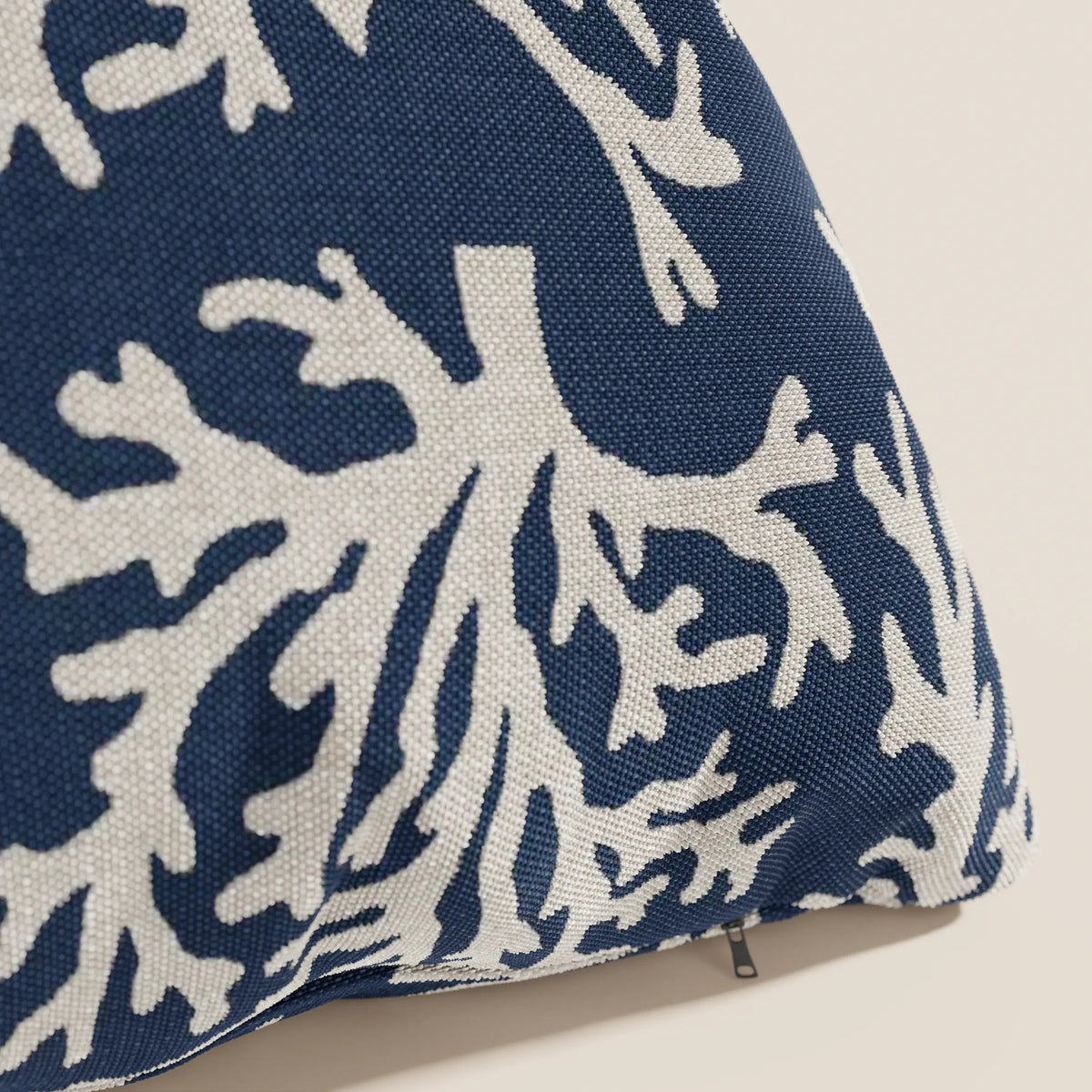 Primo piano di un cuscino Nautilus di divitt.sbs in tessuto impermeabile blu con motivo di barriera corallina bianca, che mostra una texture visibile e una cerniera aperta sul bordo. Sfondo chiaro a tinta unita.