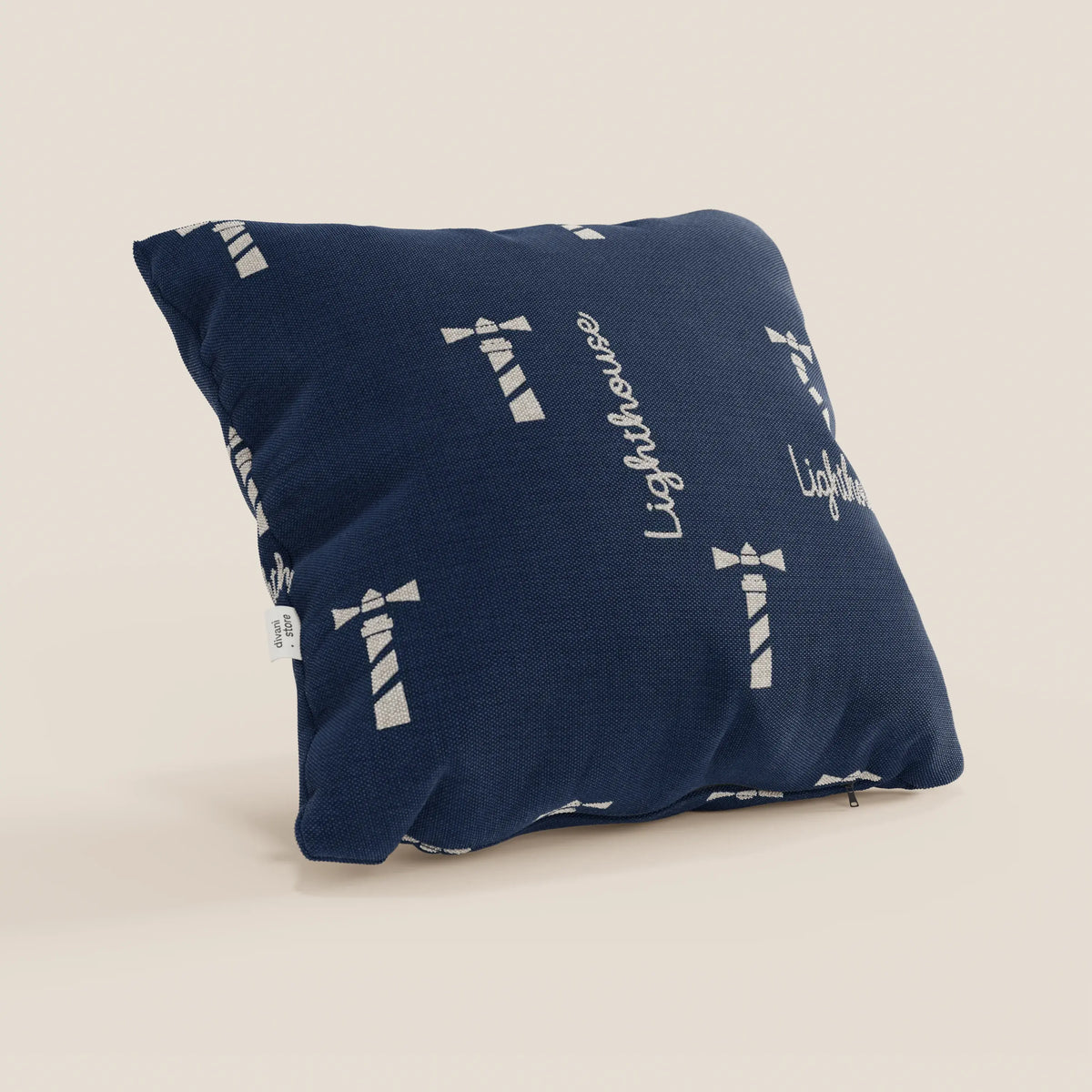 Nautilus collezione di cuscini stile marino di divitt.sbs: cuscino quadrato blu navy in tessuto impermeabile faro, con illustrazione di un faro bianco, "Lighthouse" in corsivo, una piccola etichetta laterale bianca e cuscino lavabile. Esposto su sfondo beige.
