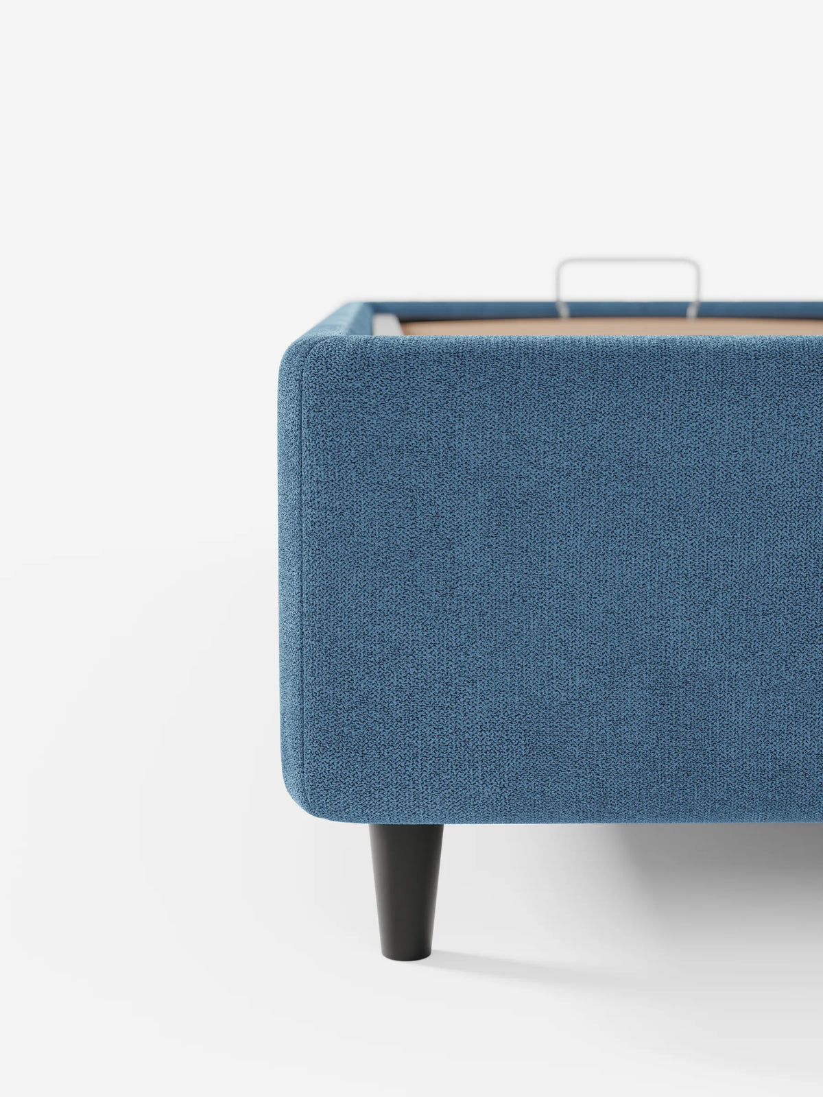 Un primo piano di un letto sommier blu ERON imbottito con vano contenitore in tessuto impermeabile certificato Oeko-Tex, caratterizzato da angoli arrotondati, gambe affusolate di colore scuro e una maniglia in metallo argentato per sollevare il vano contenitore.