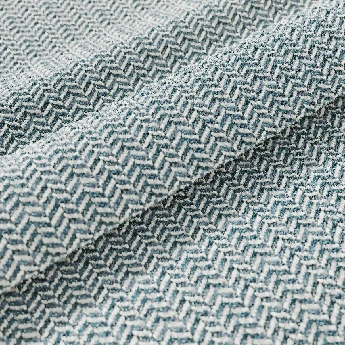Primo piano del cuscino Sorrento 45x45 in lino di divitt.sbs, caratterizzato da un motivo a zigzag chevron nei toni dell’azzurro e del bianco, ideale per l’uso all’aperto. Le morbide pieghe mettono in risalto la trama di alta qualità e l’elegante disegno geometrico.