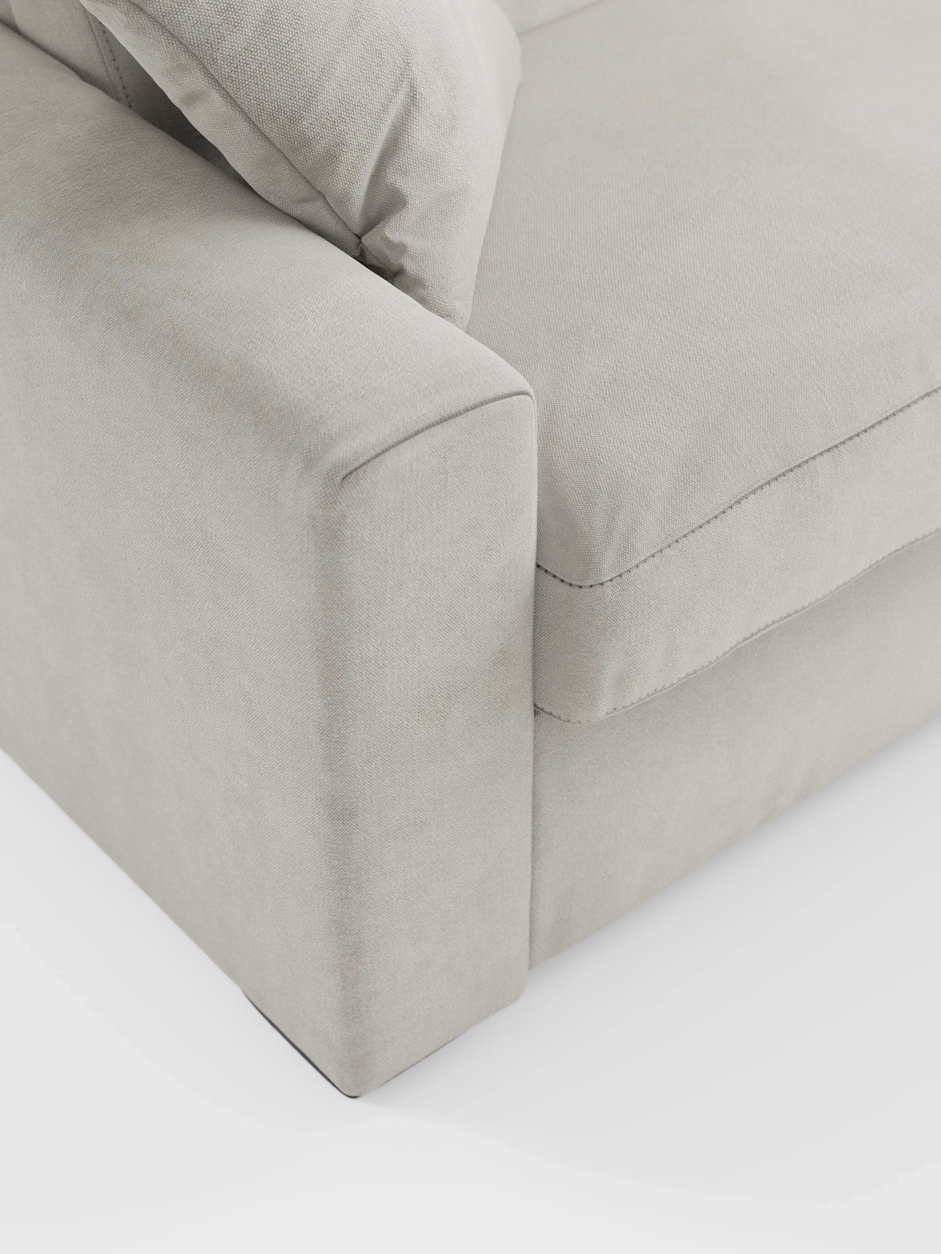 Primo piano del divano letto Maximus a 3 posti con materasso ALTO 20 cm di divitt.sbs, presentato in tessuto beige chiaro Oeko-Tex antimacchia. Il divano presenta braccioli ampi e squadrati, seduta imbottita con cuciture a vista e poggiatesta regolabili. L'immagine mette in risalto la morbida trama del rivestimento e le linee pulite su uno sfondo bianco.