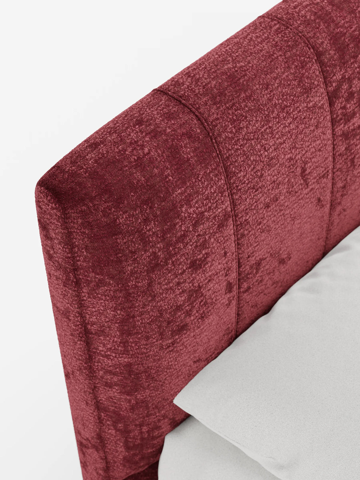 Un primo piano di un divano letto ONYX color bordeaux con vano contenitore e testiera verticale in tessuto certificato Oeko-Tex®, con trapuntatura a canali verticali, su sfondo bianco accanto a un cuscino grigio chiaro a tinta unita.