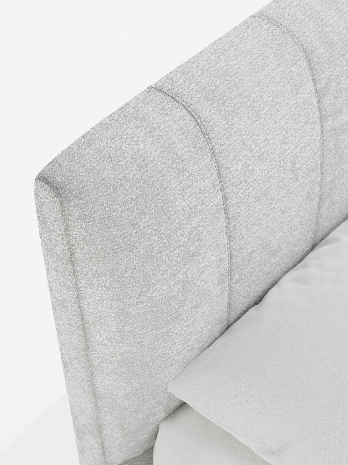 Un primo piano dell'angolo di un letto imbottito ONYX con contenitore e testiera verticale in tessuto certificato Oeko-Tex®, caratterizzato da una trapuntatura a canali verticali di colore grigio chiaro e da un tessuto testurizzato in tinta, in contrasto con un cuscino grigio.