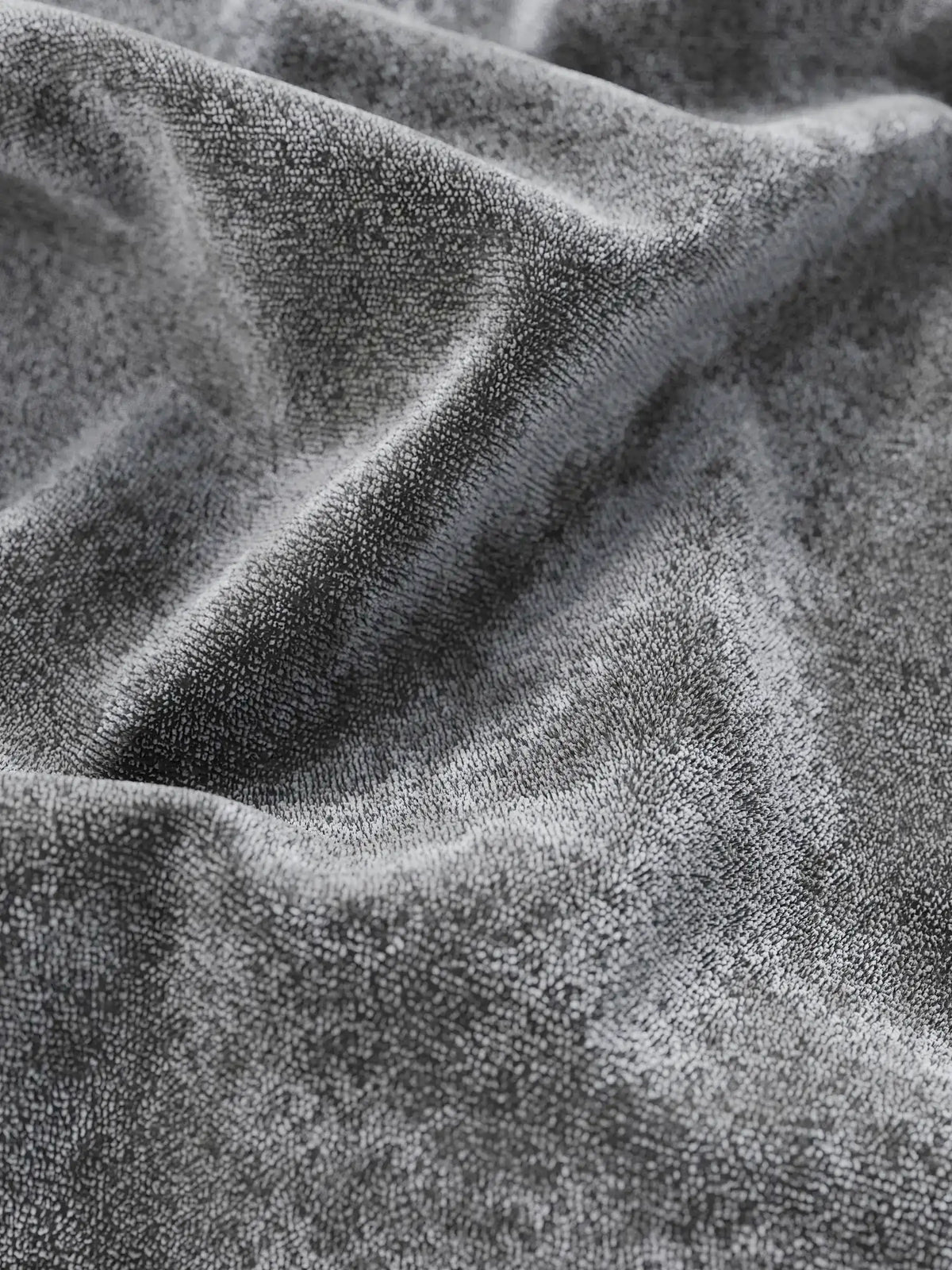Primo piano sul tessuto grigio scuro, morbido e dalla trama ricca di un letto imbottito AURO con vano contenitore e testiera capitonné alta in ciniglia Oeko-Tex®, caratterizzato da pieghe profonde che riflettono la luce e da un effetto ondulato e tridimensionale.