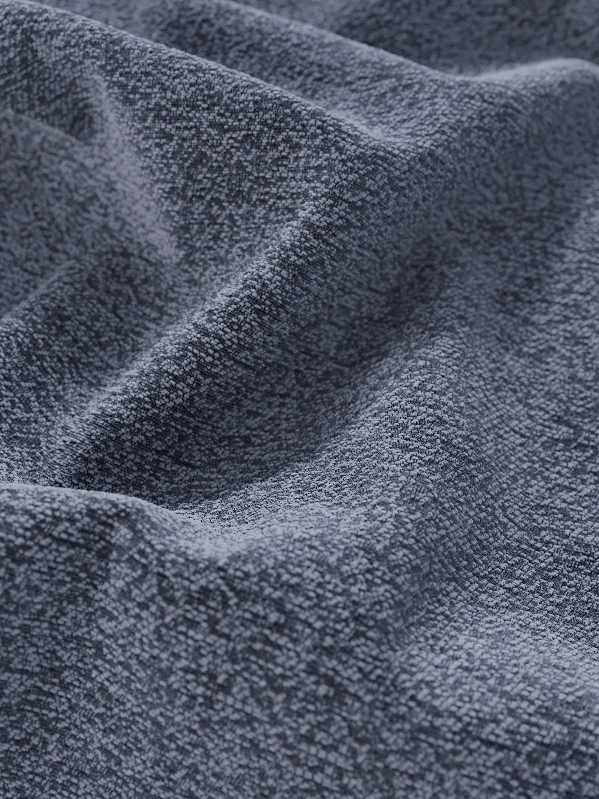 Primo piano del letto di design VALKIRIA con vano contenitore e testiera avvolgente, realizzato in tessuto grigio scuro caratterizzato da morbide e profonde pieghe e da un motivo intrecciato fitto.