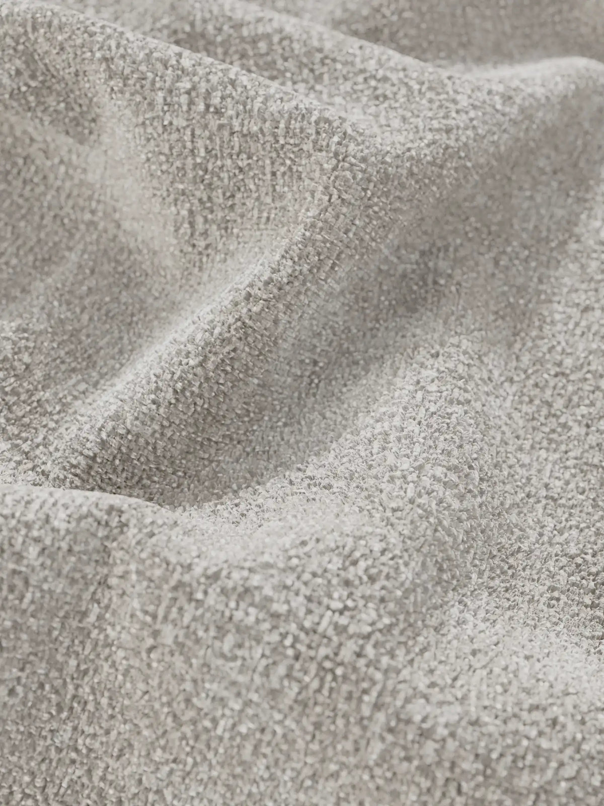 Primo piano sul tessuto grigio chiaro e materico di un divano letto Ottaviano con letto estraibile - penisola reversibile e contenitore in tessuto materico lavabile, con pieghe profonde che ne sottolineano la trama spessa, simile al bouclé.