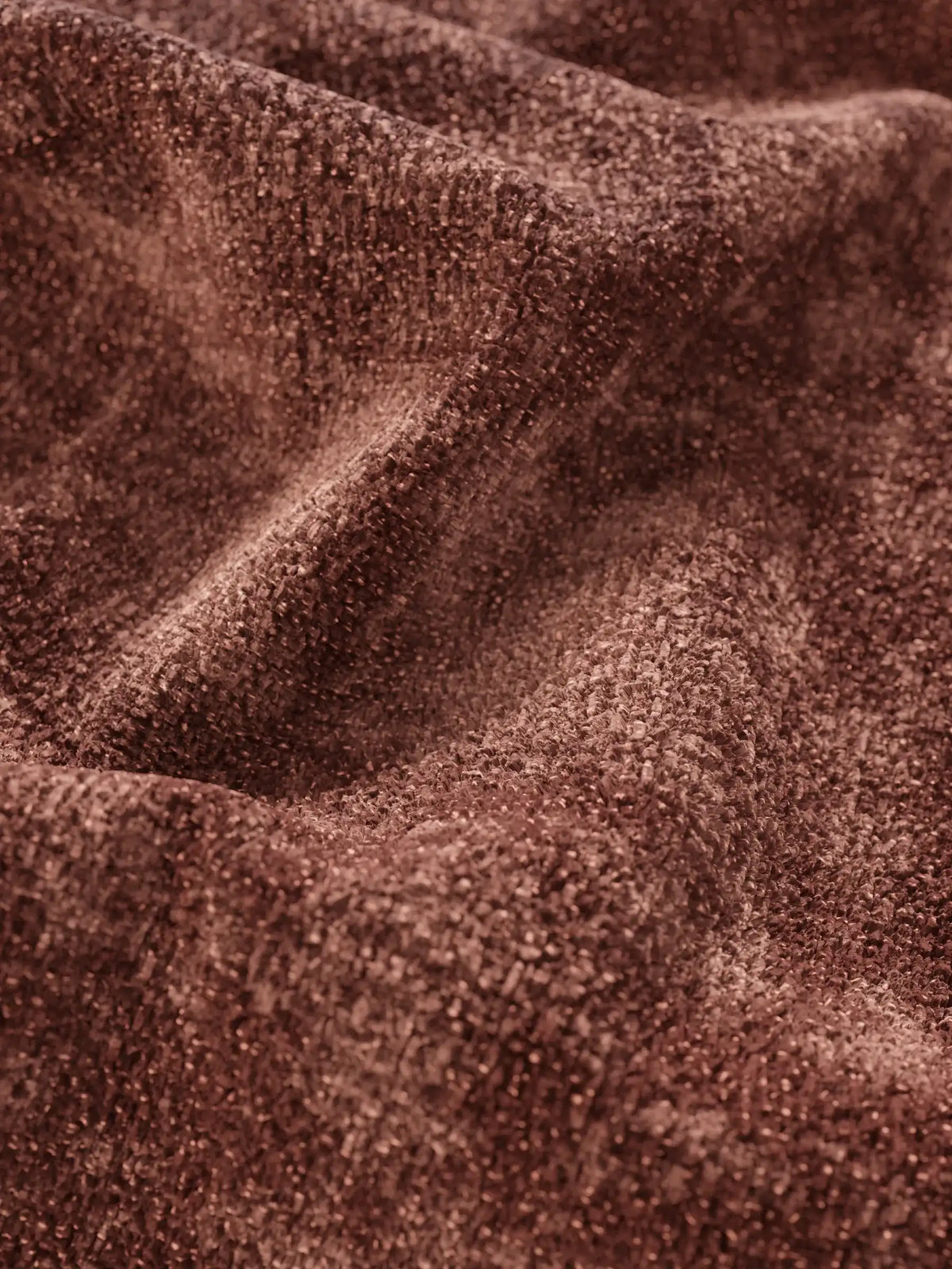 Primo piano di un tessuto materico dal colore rosso-marrone intenso, drappeggiato in morbide pieghe su un divano letto Ottaviano con letto estraibile – penisola reversibile e contenitore in tessuto materico lavabile, caratterizzato da una superficie intrecciata, leggermente luccicante e compatta.