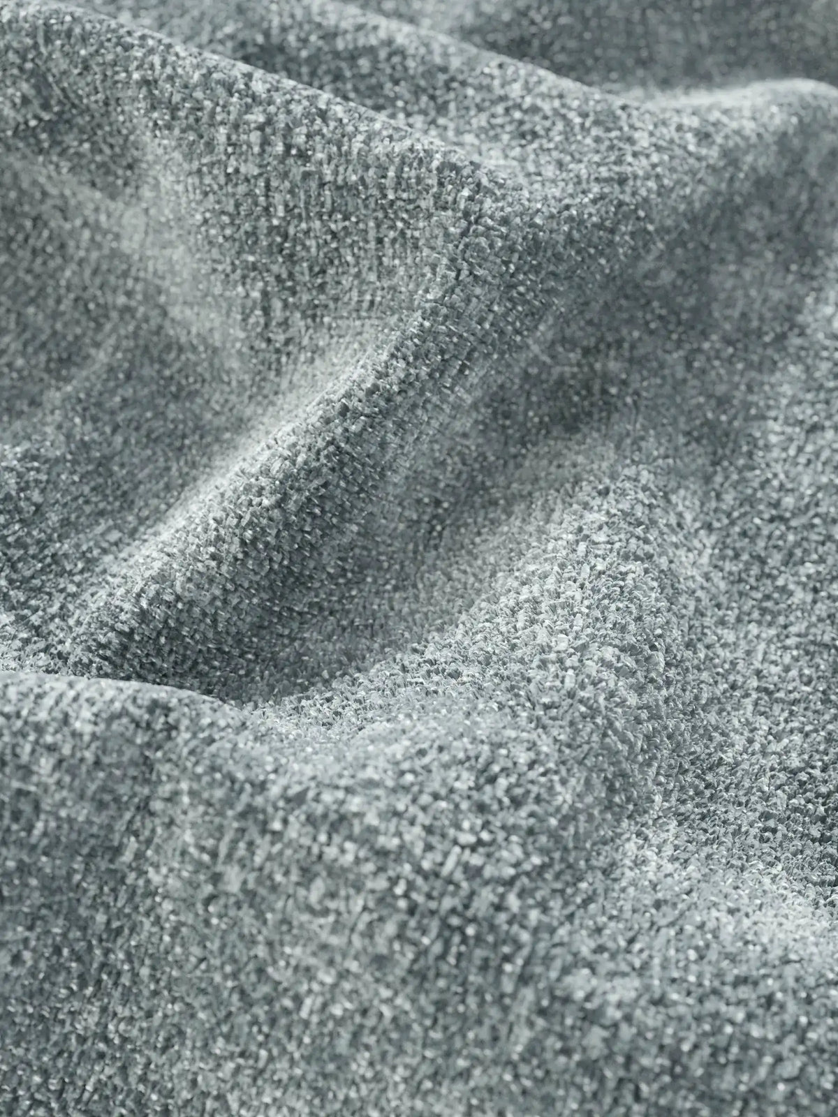 Primo piano del tessuto grigio-argento a trama rigata del divano letto con letto estraibile Ottaviano, che presenta morbide e profonde pieghe che creano un gioco di luci e ombre sulla superficie intrecciata.