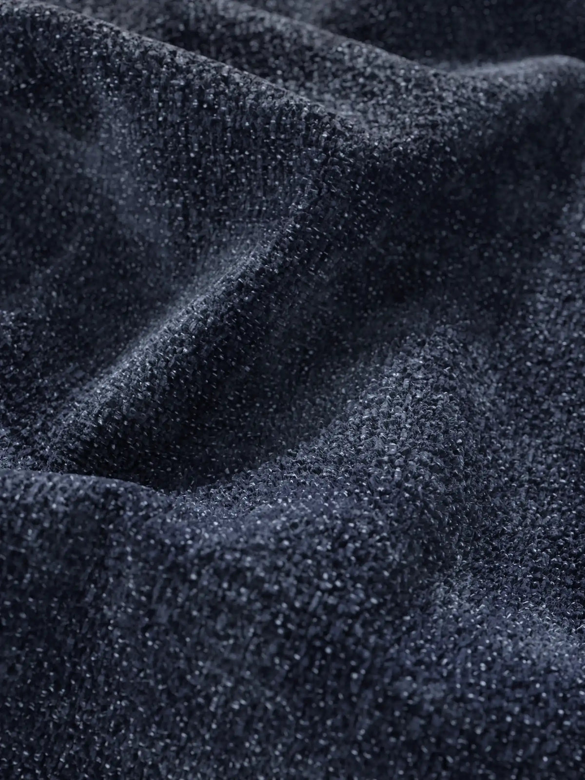Primo piano del rivestimento in tessuto blu navy scuro a trama ruvida del divano letto Ottaviano con letto estraibile – penisola reversibile e contenitore in tessuto materico lavabile, che mostra morbide pieghe e una trama ruvida e granulosa con una leggera lucentezza.