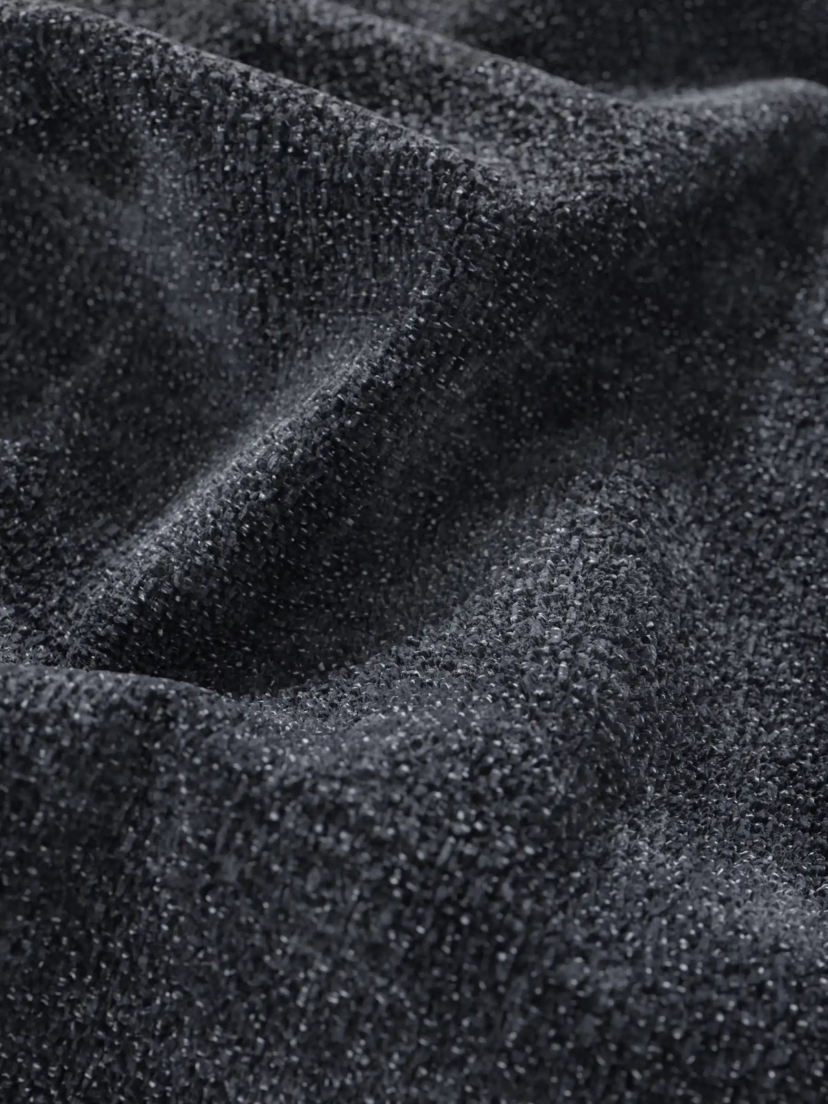 Un primo piano del tessuto intrecciato grigio scuro del divano letto Ottaviano con letto estraibile – penisola reversibile e contenitore in tessuto materico smacchiabile, che mostra pieghe strutturate con una superficie granulosa e sottili riflessi di luce.
