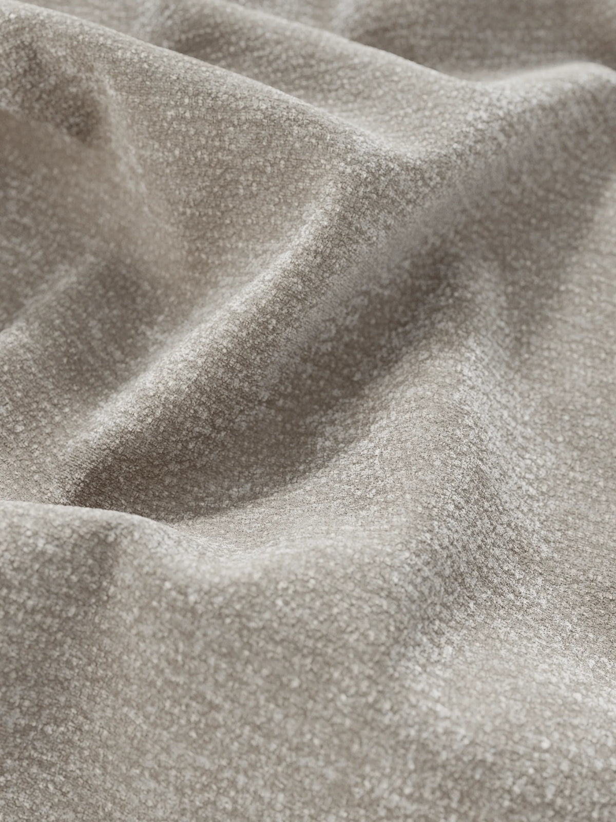 Primo piano del tessuto color taupe dalla trama ruvida su un letto imbottito ONYX con contenitore e testiera verticale in tessuto certificato Oeko-Tex®, che presenta morbide pieghe e una trama granulosa con sottili giochi di luce e ombra.