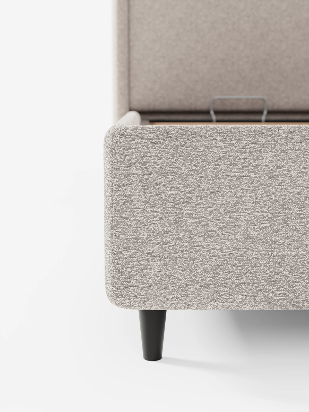 Una vista parziale del letto di design VALKIRIA con vano contenitore e testiera avvolgente in tessuto grigio chiaro testurizzato, caratterizzato da un angolo arrotondato, una gamba corta e conica di colore scuro e una base aperta con maniglia in metallo a vista.