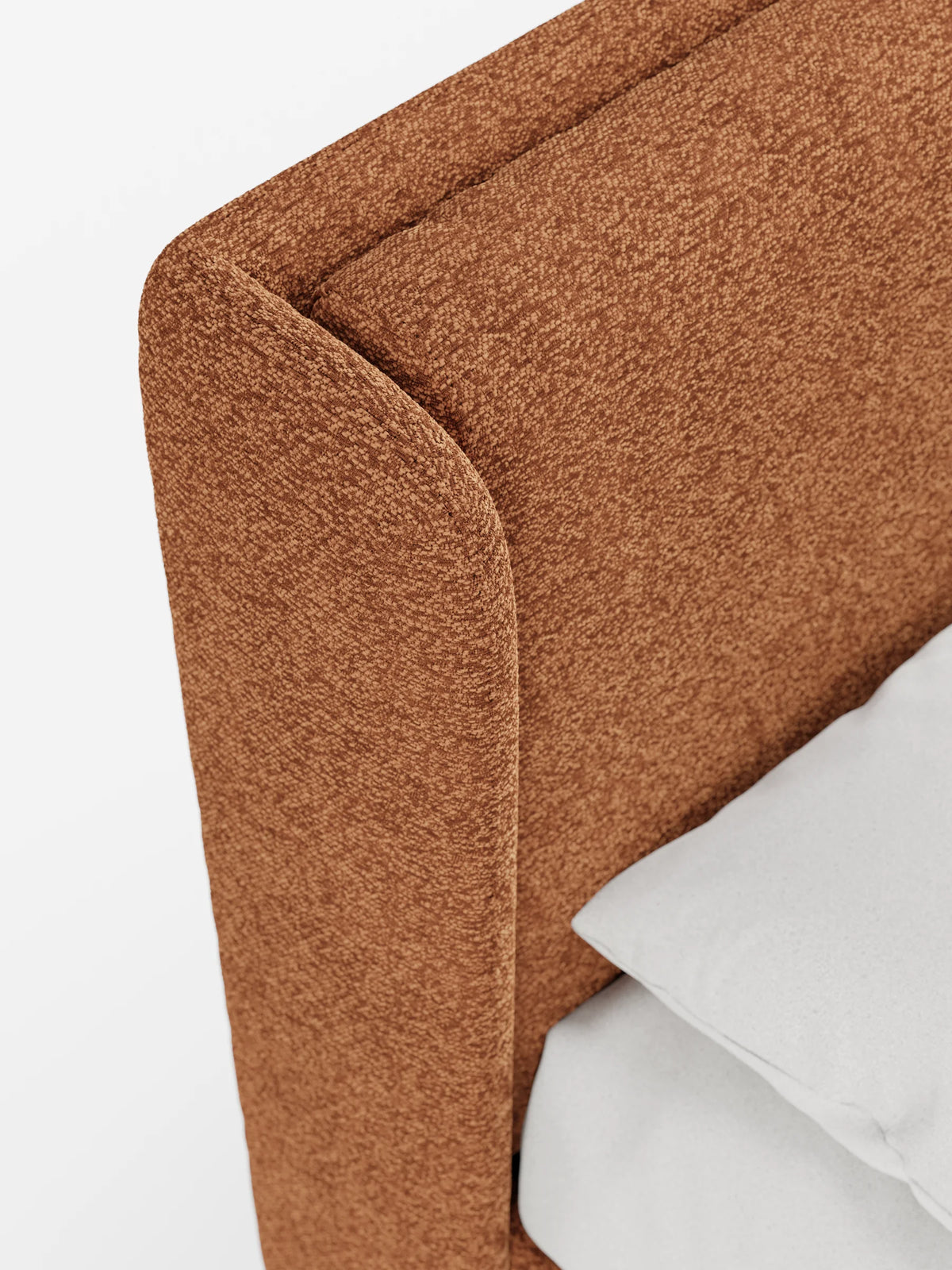 Un primo piano del letto di design VALKIRIA con contenitore e testiera avvolgente, caratterizzato da una testiera curva in tessuto color cognac con trama a rilievo, con un cuscino grigio chiaro appoggiato al pannello laterale arrotondato.