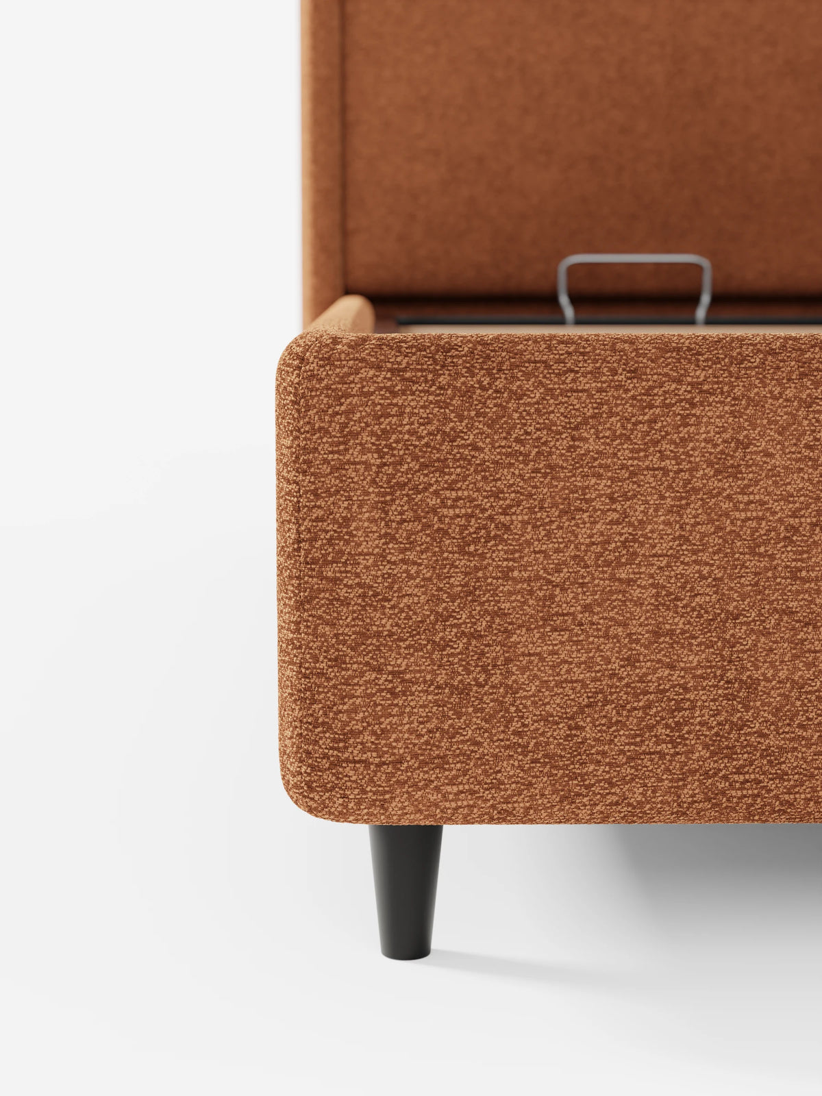 Un primo piano del letto di design VALKIRIA con vano contenitore e testiera avvolgente - 2 cuscini imbottiti e tessuto Oeko-Tex®: struttura rivestita in arancione ruggine con angoli arrotondati, gambe affusolate e vano contenitore aperto.
